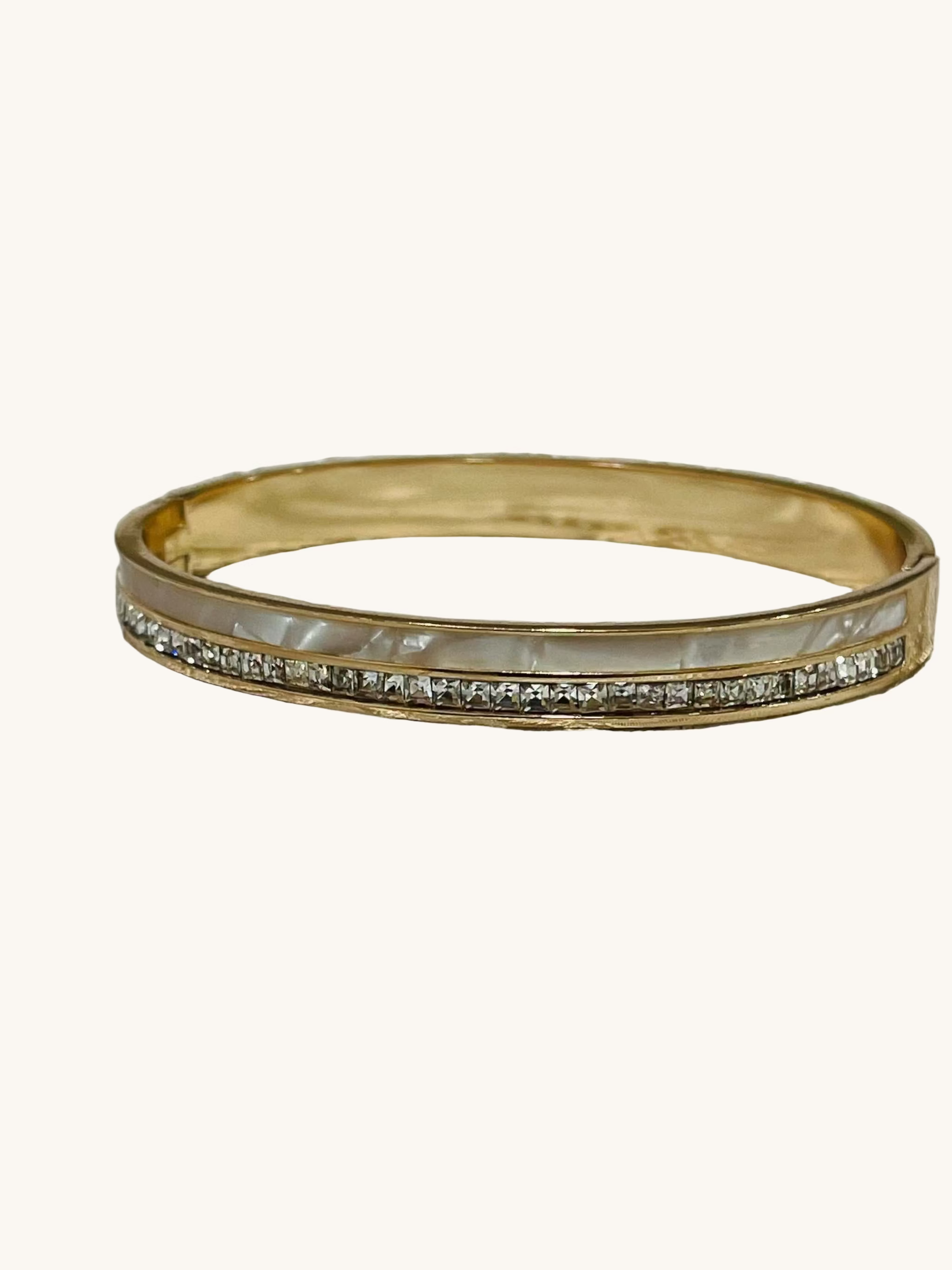 Gold bracelet featuring mother of pearl inlay and a row of sparkling American diamonds on intricate fabric background