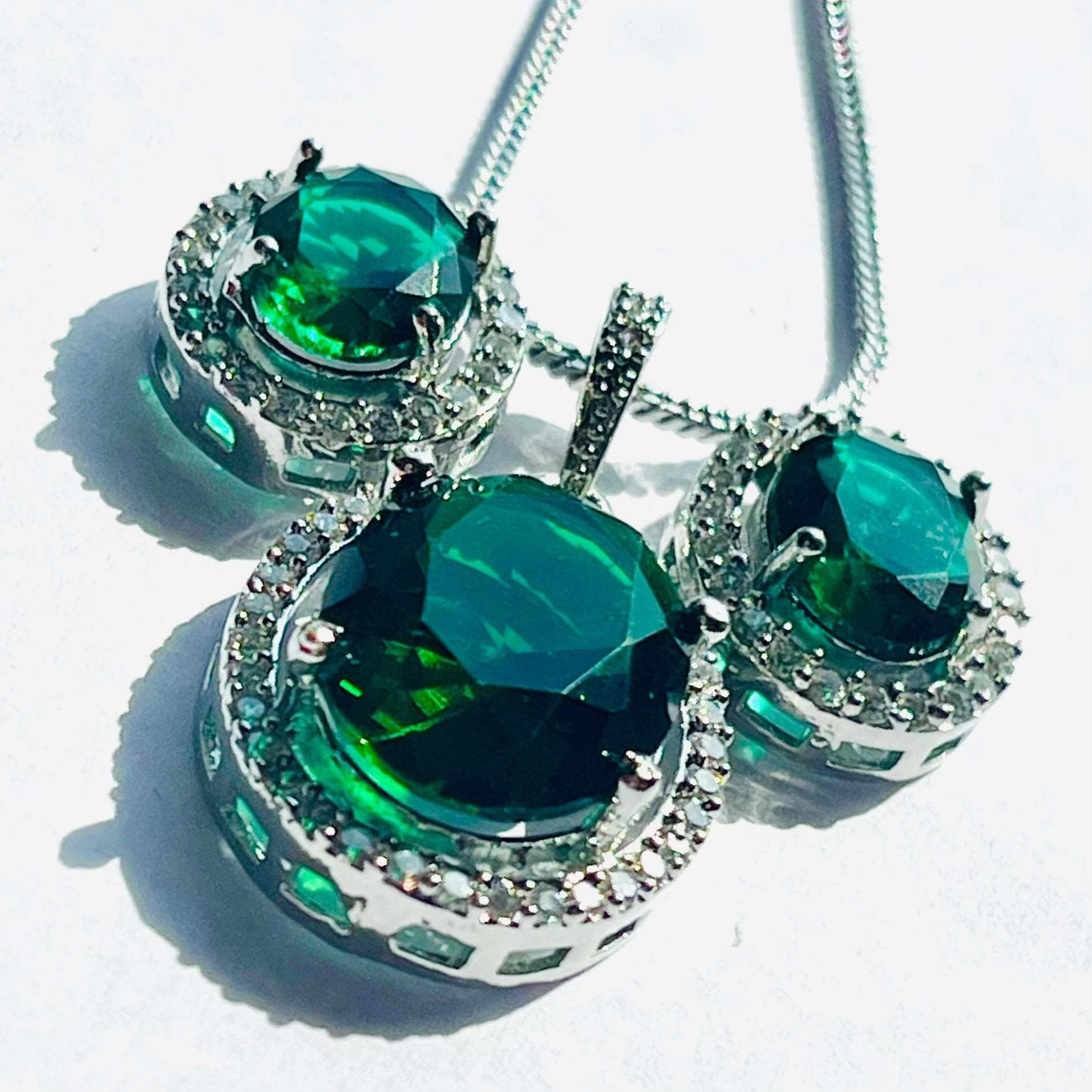 Emerald grand pendant set with oval green stones surrounded by white diamonds on silver chain