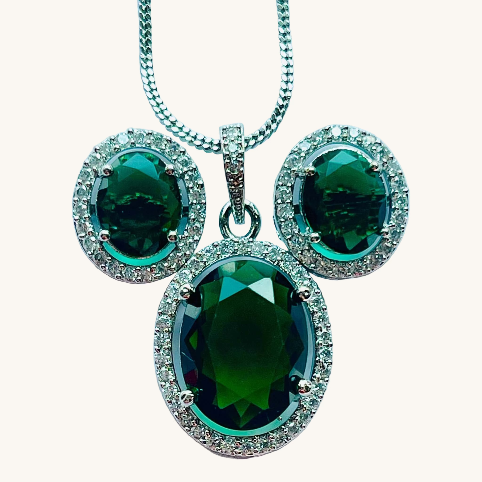 Emerald grand pendant set with oval emerald stones surrounded by white diamonds in silver setting