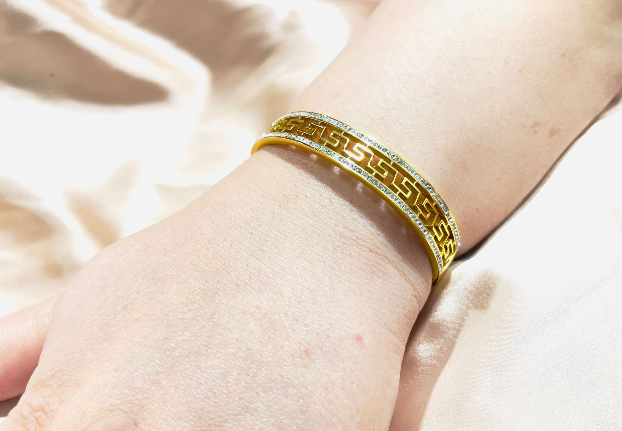 Hand wearing a geometric gold bracelet with intricate design and rose gold finish on a light fabric background
