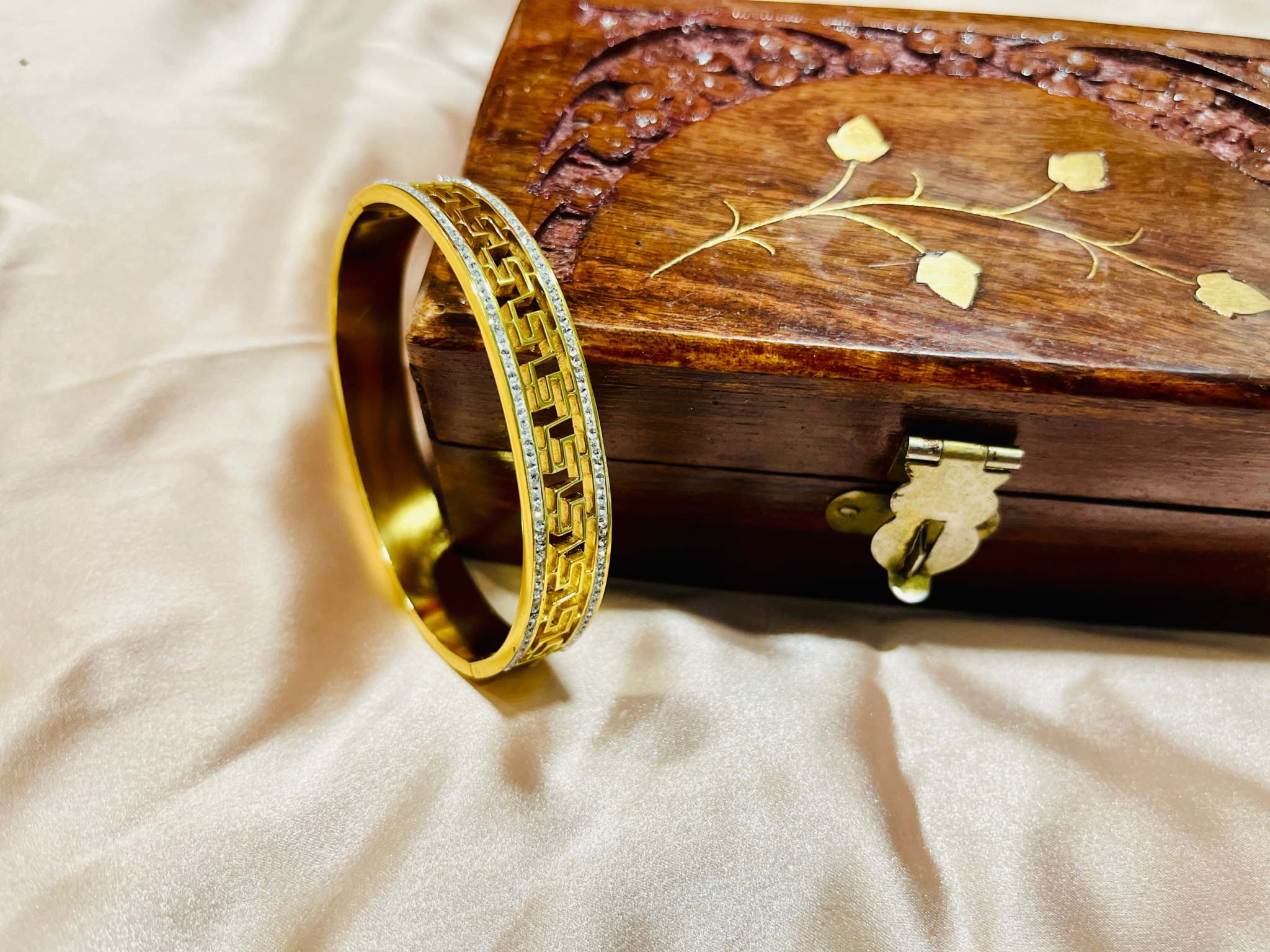 Geometric gold bracelet with intricate cut-out design displayed on a carved wooden box