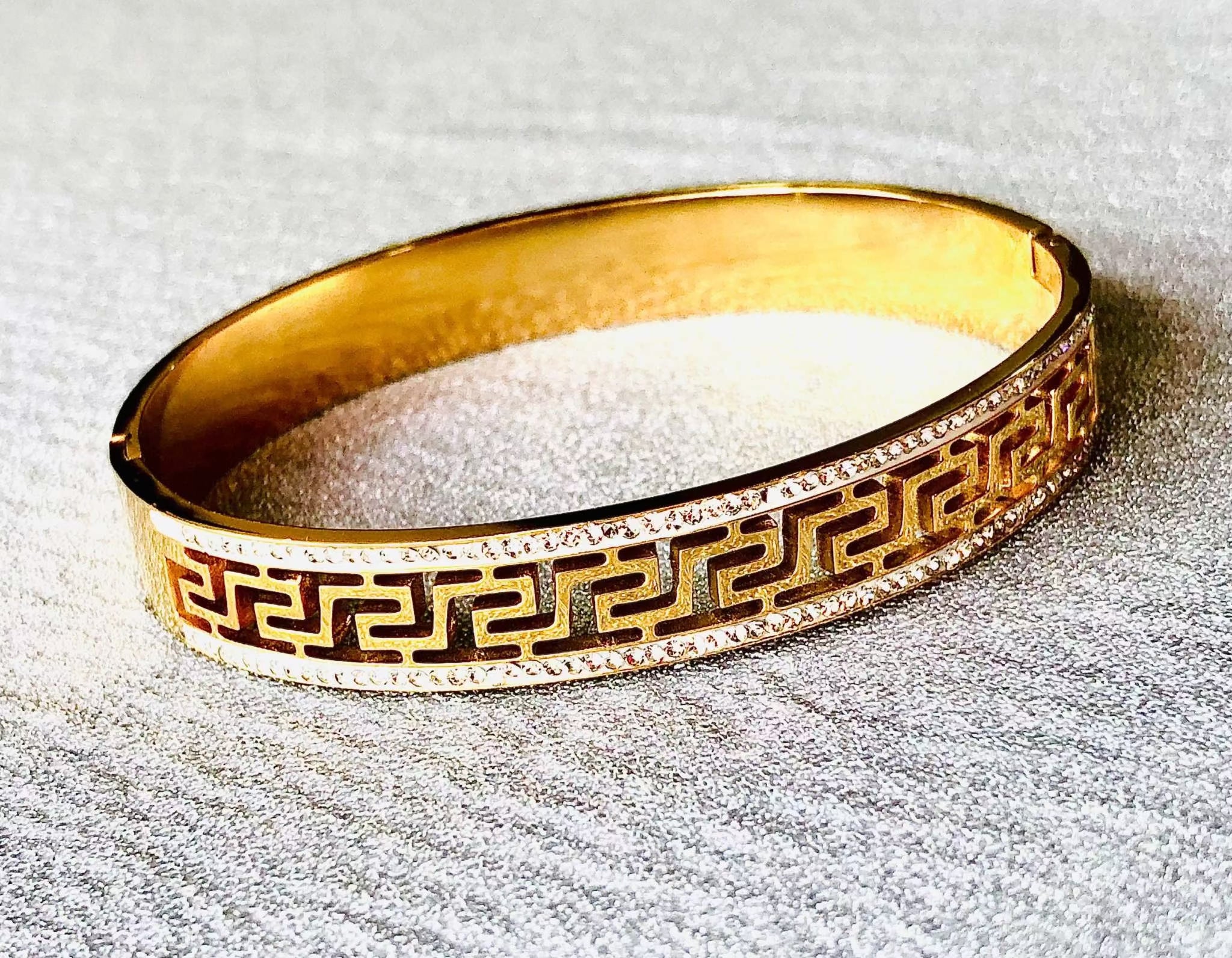 Geometric gold bracelet with intricate cutout pattern and polished finish on textured surface