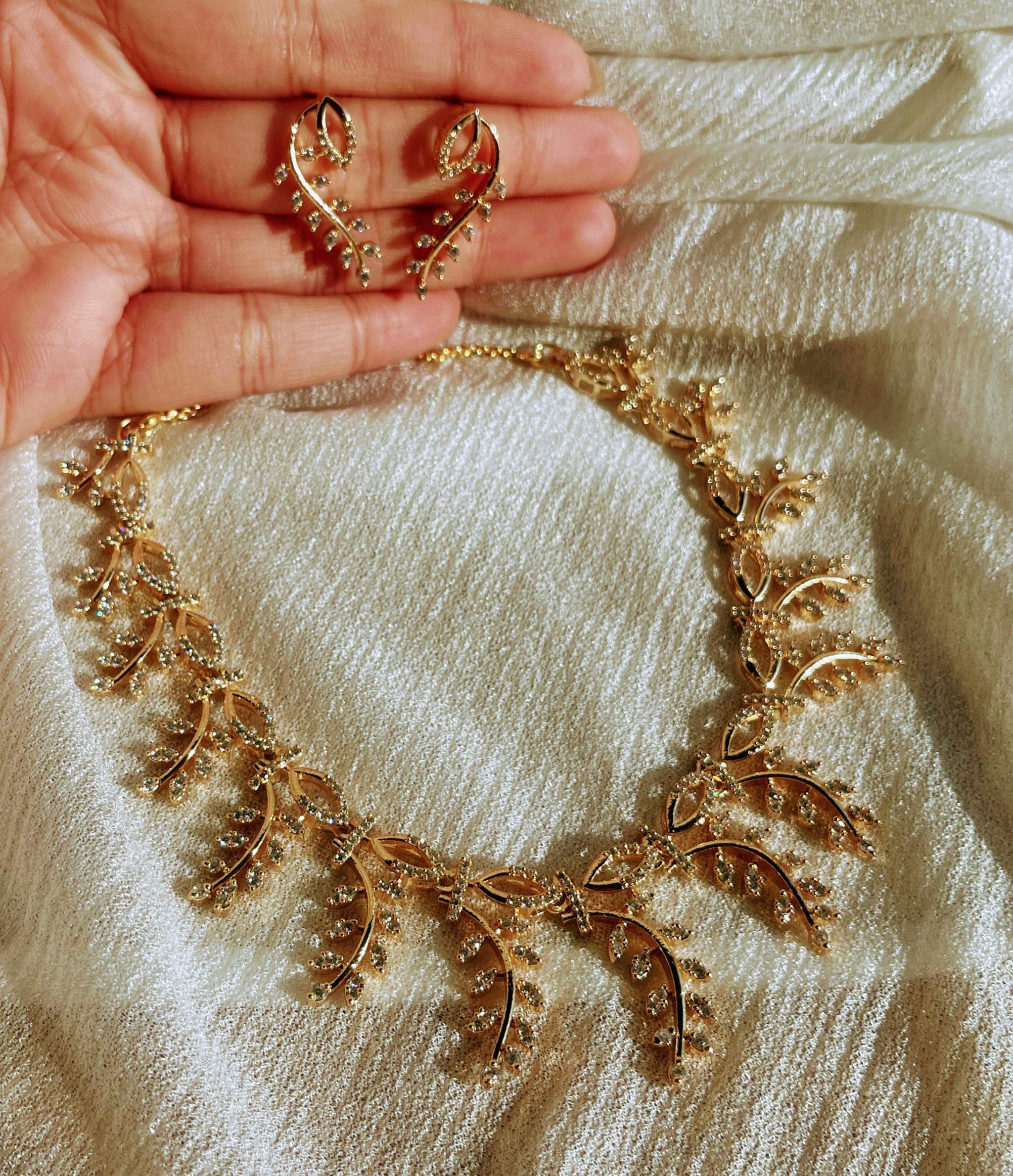 Everglow Willow Necklace Set in gold with delicate leaf design and matching earrings on fabric background