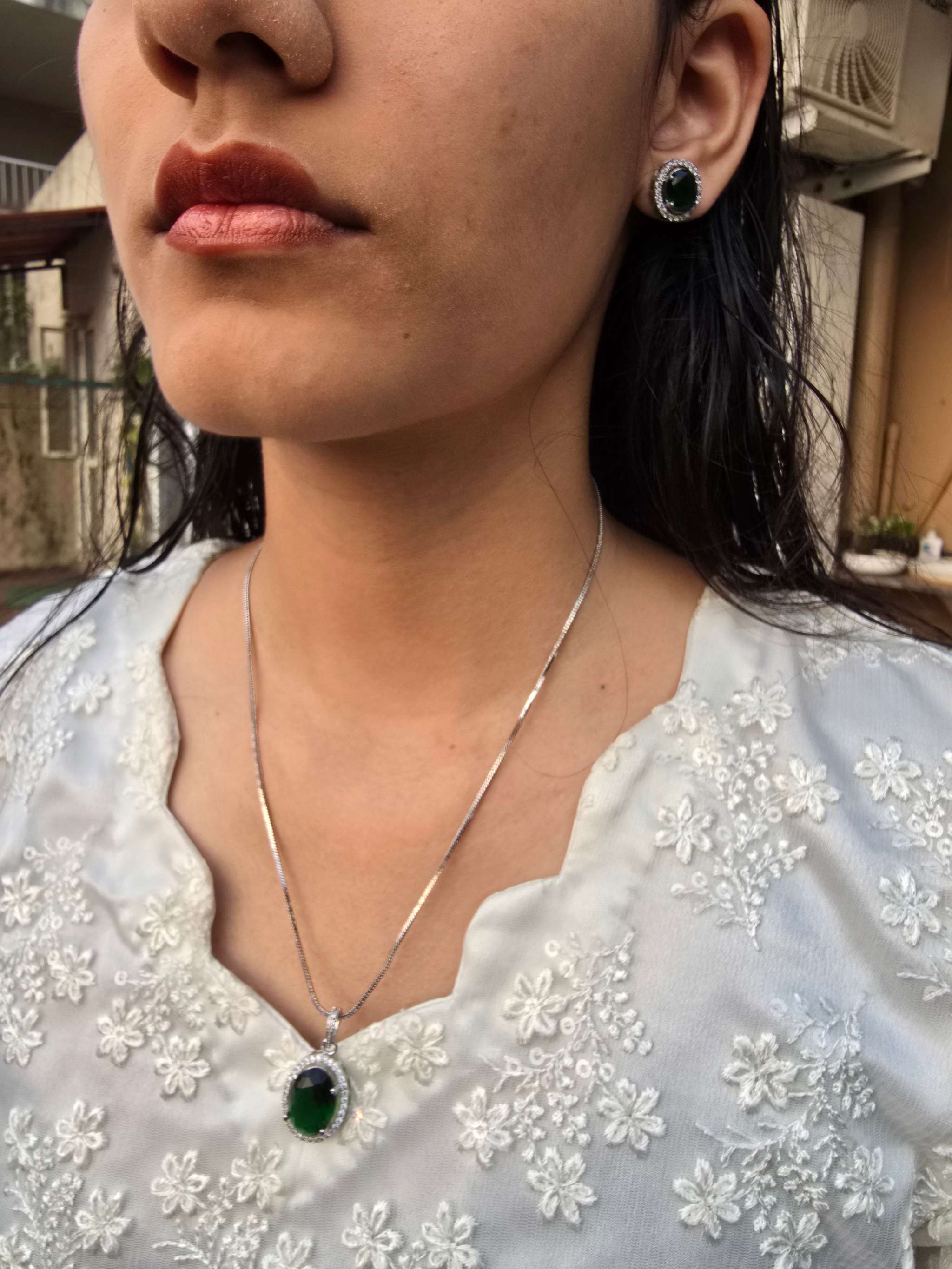 woman wearing violet oval grand pendant necklace and matching earrings with white floral embroidered top outdoors