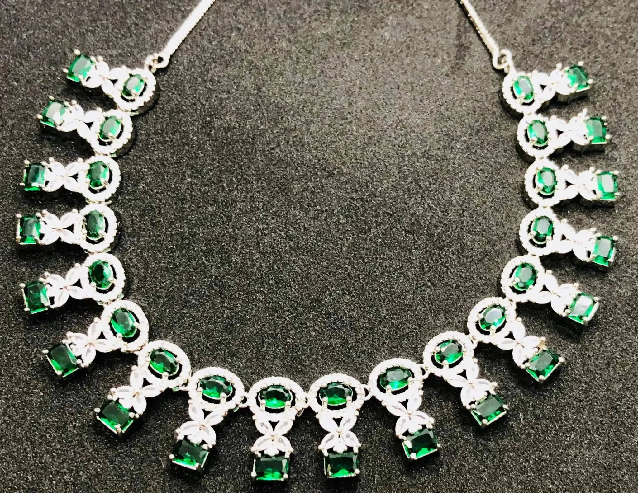 Radiant emerald necklace set featuring vibrant green gemstones and intricate silver detailing on a black background