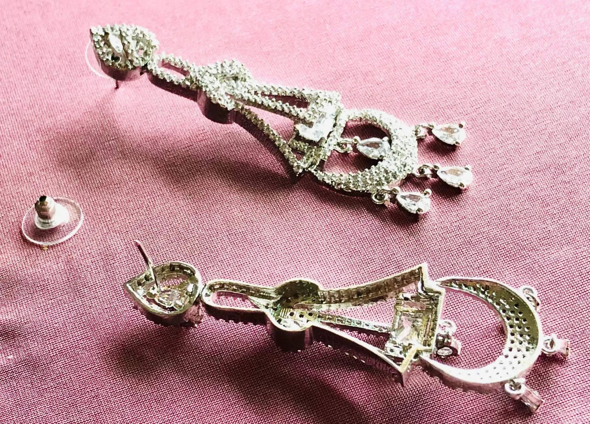Silver and white diamond dangling earrings with intricate design on pink fabric background
