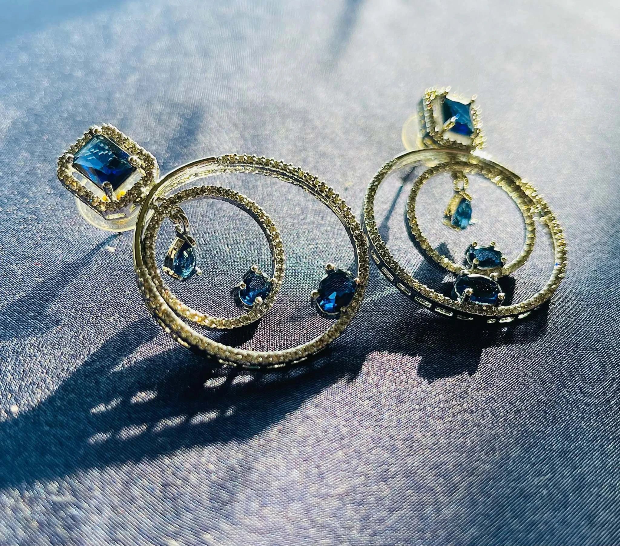 Silver hoop earrings with blue gemstone pendants and diamond accents.
