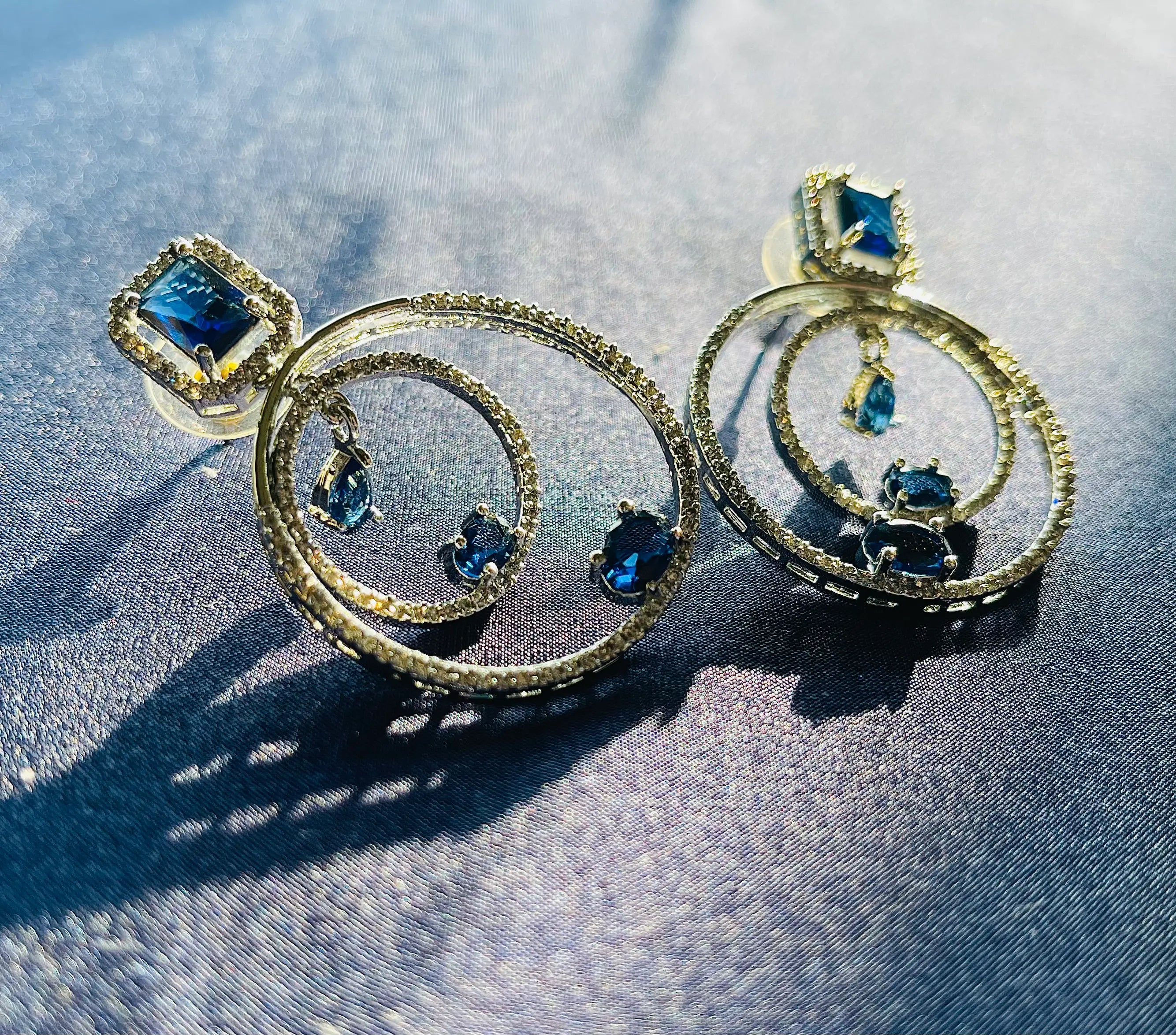 Silver hoop earrings with blue gemstone pendants and diamond accents.