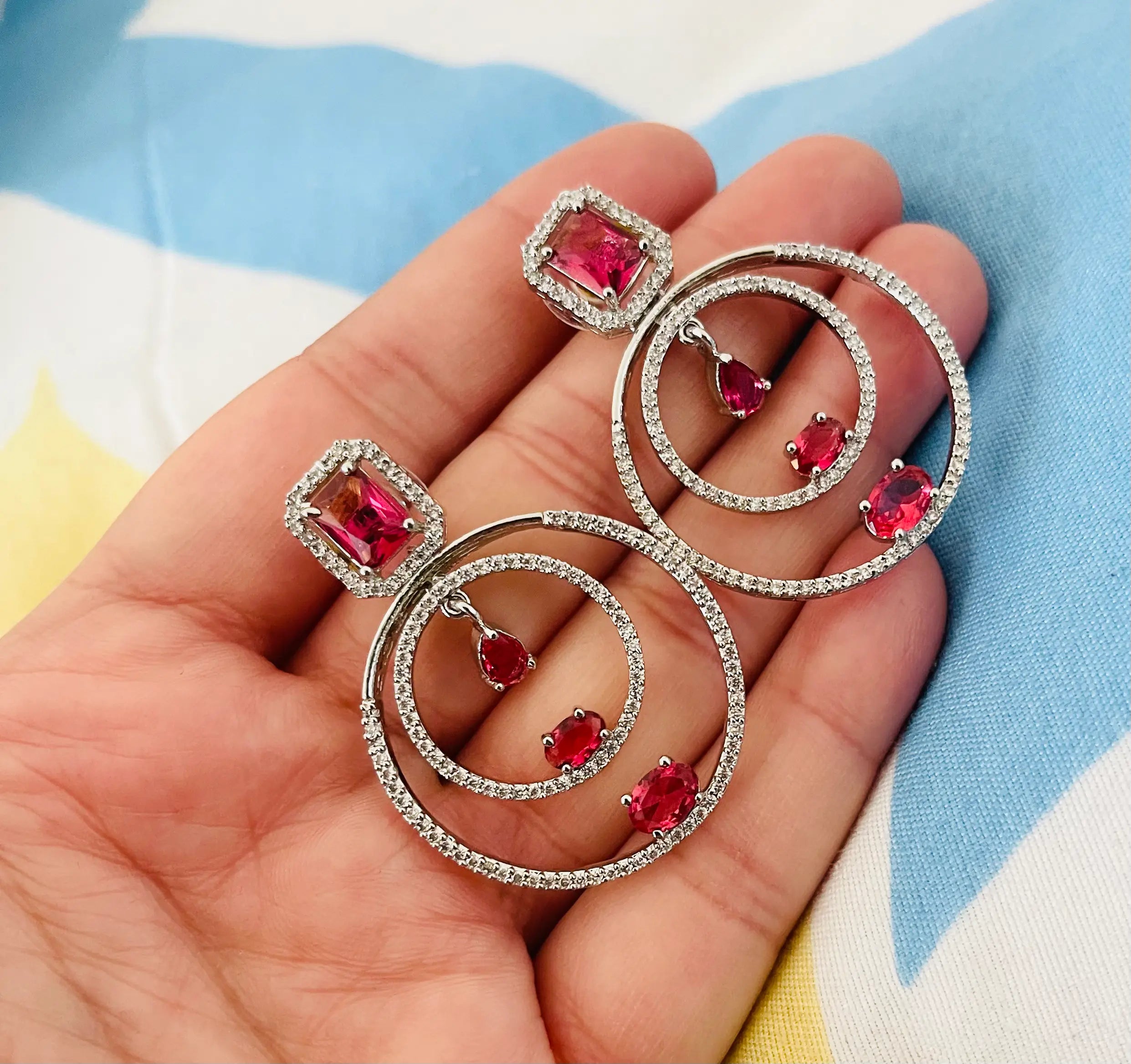 Hand holding silver spiral drop earrings with pink gemstones and diamond accents.