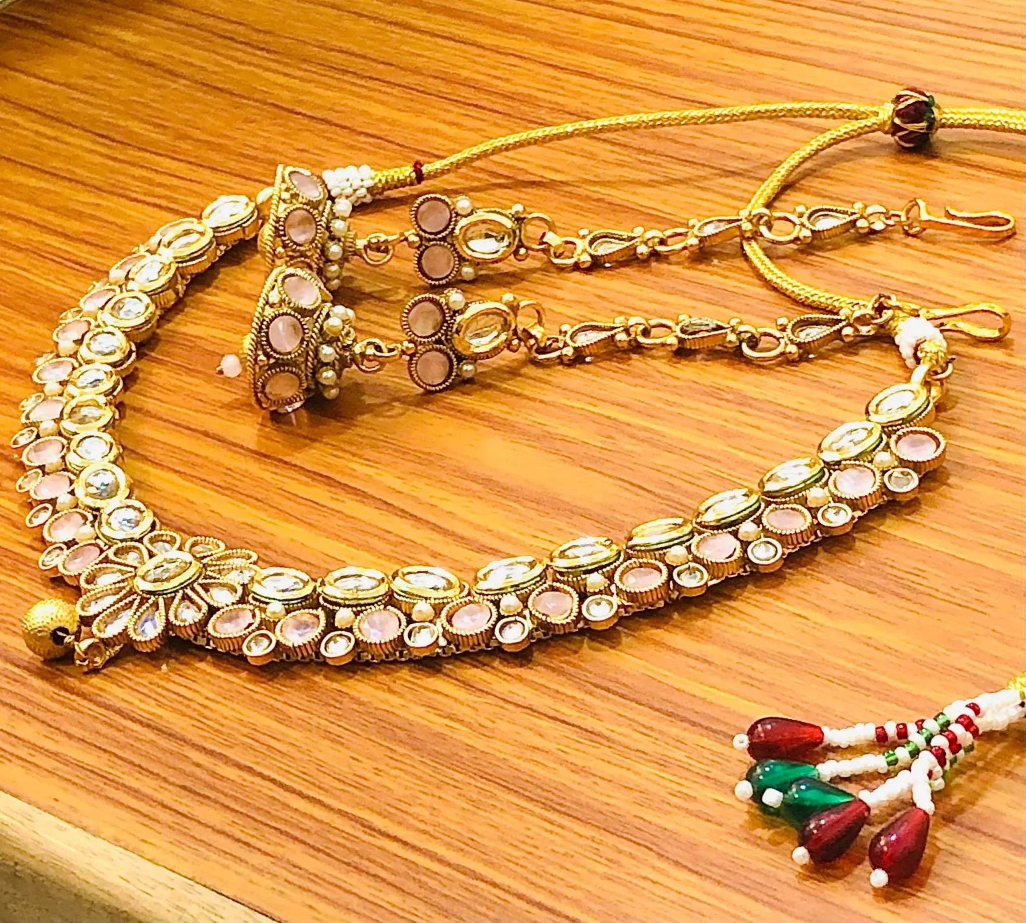 Pastel pink and golden Kundan necklace with matching intricate jhumka earrings on wooden surface