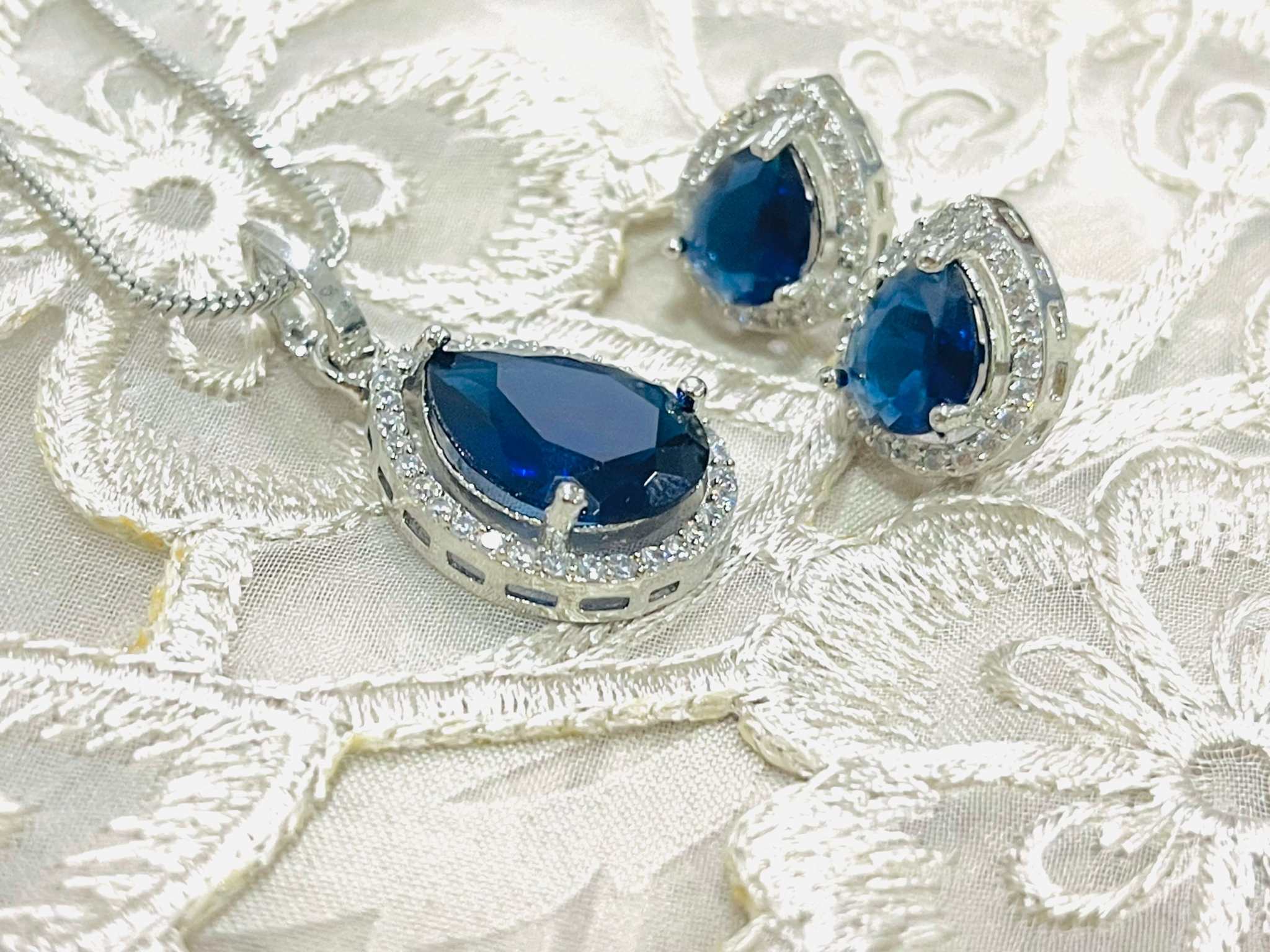 Indigo Grand Pendant Set featuring deep blue teardrop gemstones with silver detailing on lace background