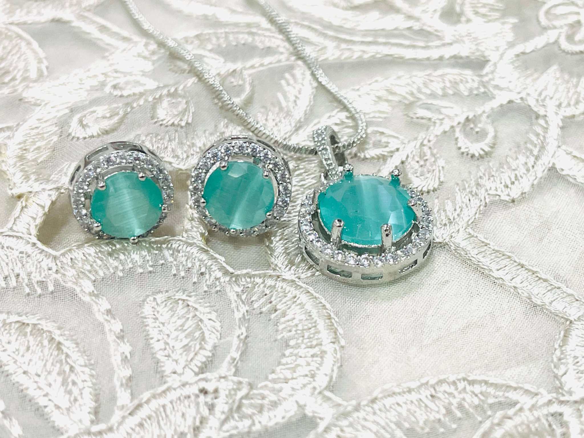 Teal Majestic Moonlit round pendant set with silver chain and matching earrings featuring AD stones on lace fabric background