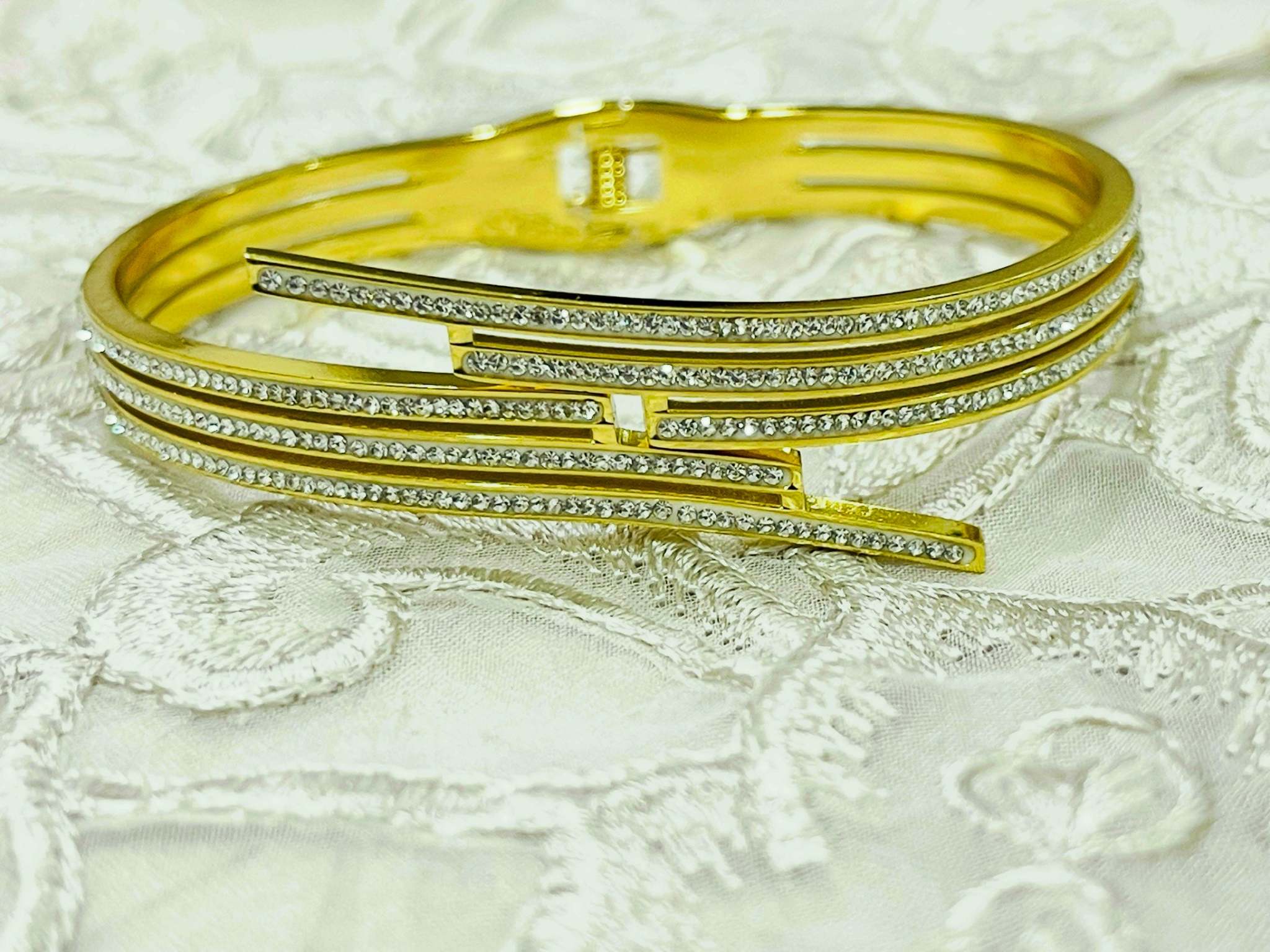 Sleek triple lines gold bracelet with sparkling stones and modern minimalist design on textured fabric background