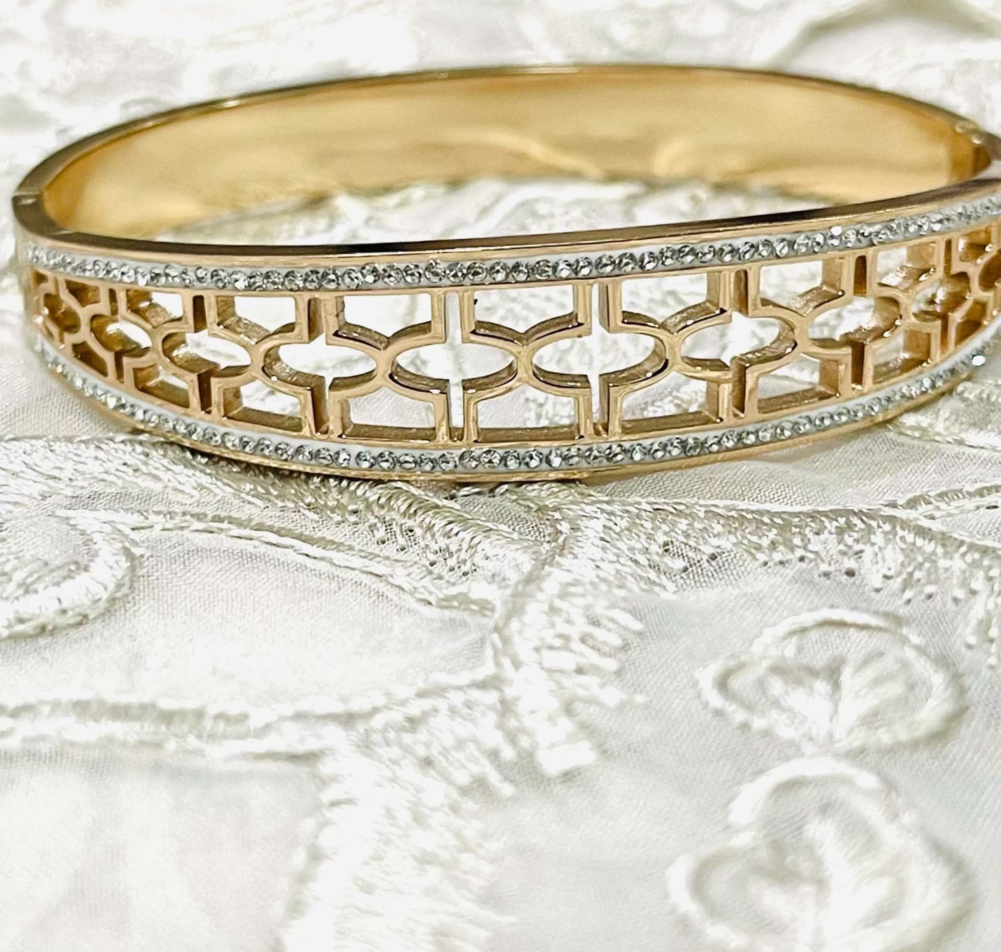 Gold bracelet with intricate jali work and embedded stones on delicate fabric background