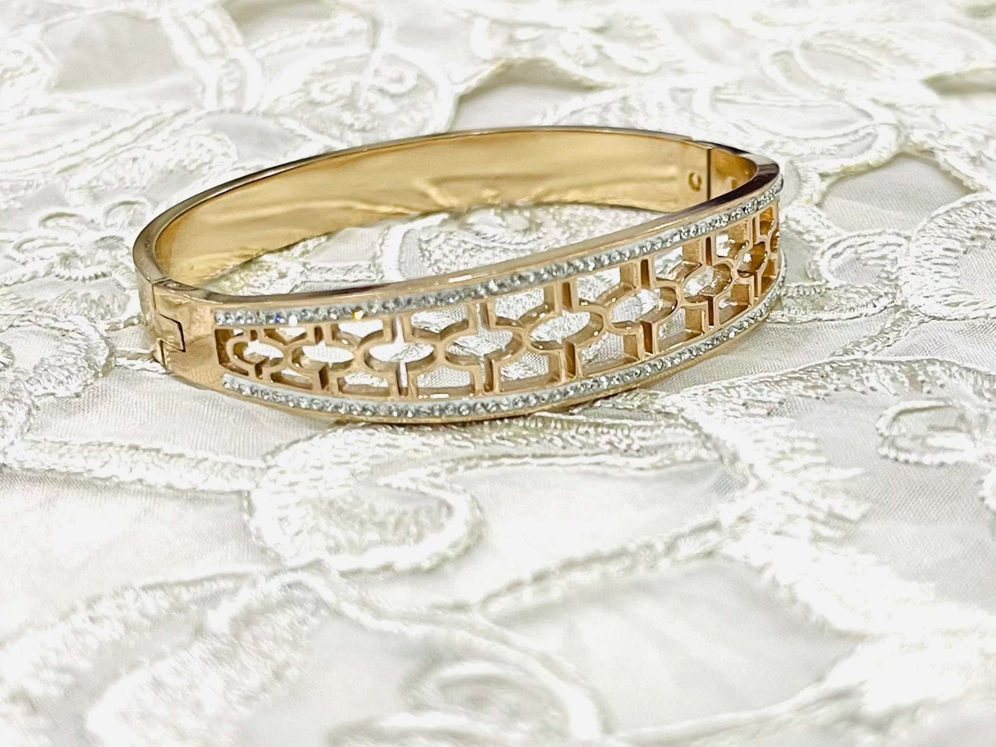 gold intricate jali work bracelet with diamond accents on white lace background
