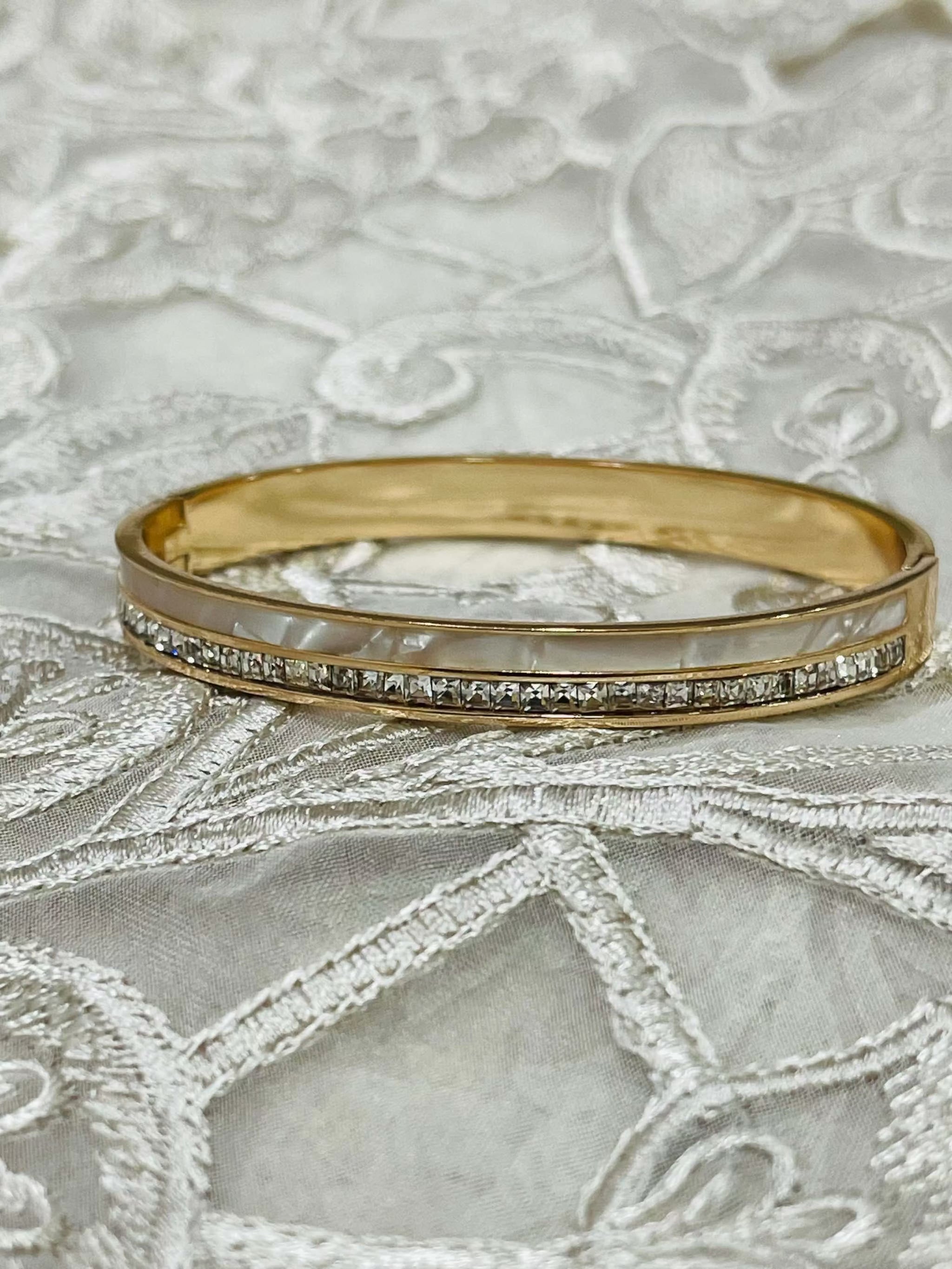 Gold bracelet featuring mother of pearl inlay and a row of sparkling American diamonds on intricate fabric background