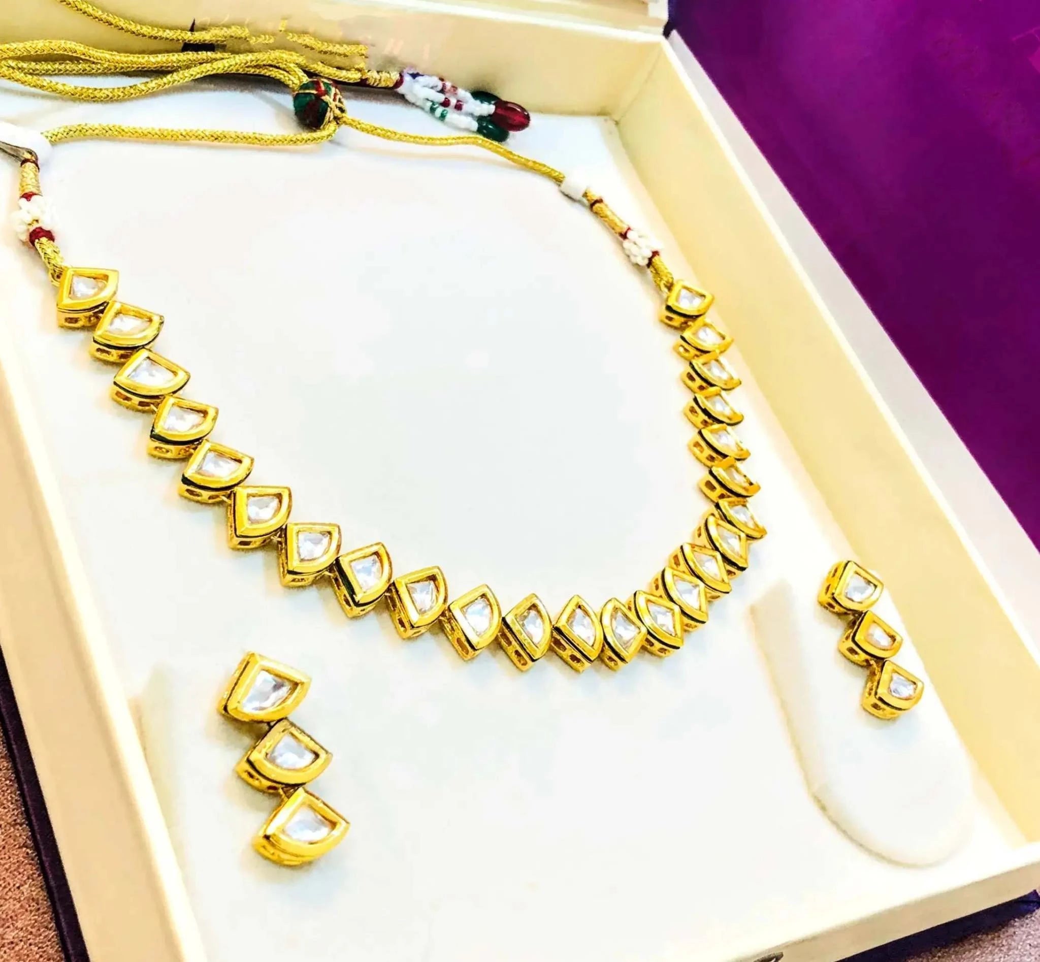Golden and white triangular kundan necklace set with matching earrings in an elegant box