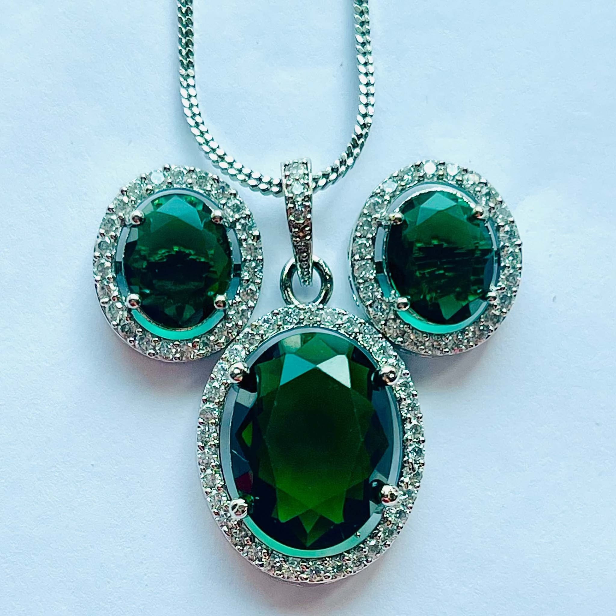 Emerald grand pendant set with oval emerald stones surrounded by white diamonds in silver setting