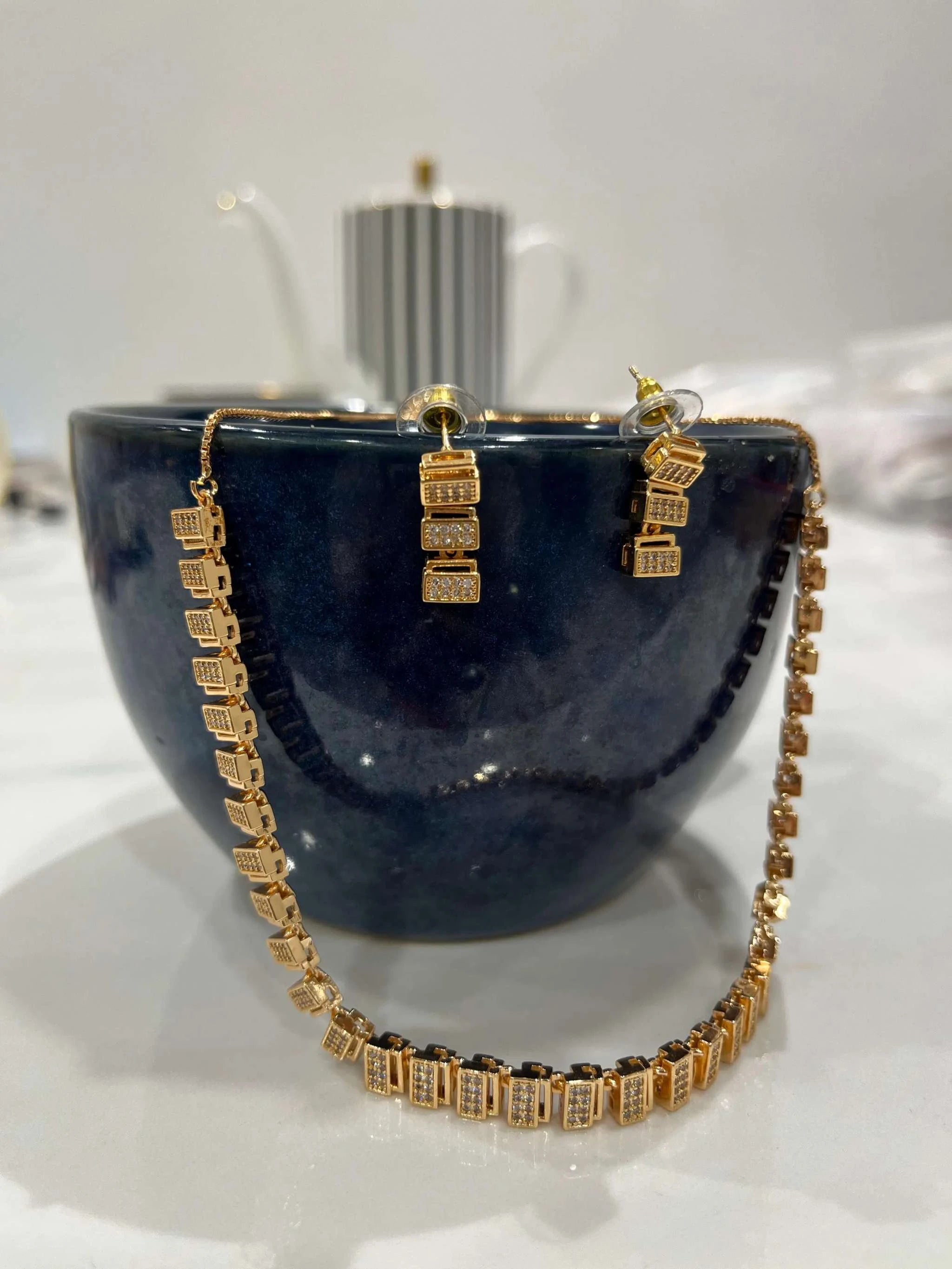 Classic rose gold zircon necklace and matching earrings set displayed on a dark cup, elegant jewelry for timeless style