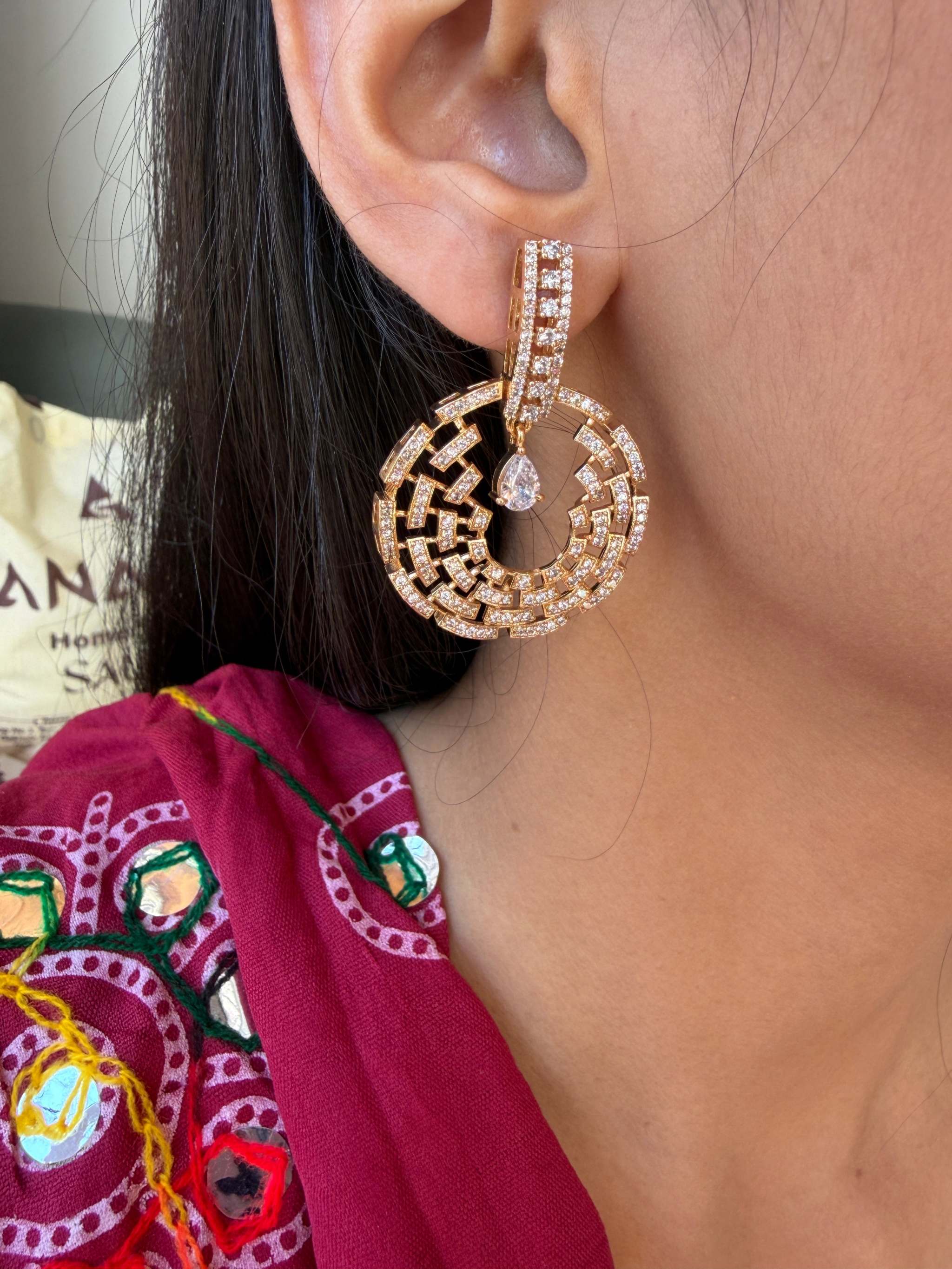 Close-up of a rose gold Celestial Maze Danglers earring with intricate maze design and a teardrop gemstone worn on a woman's ear