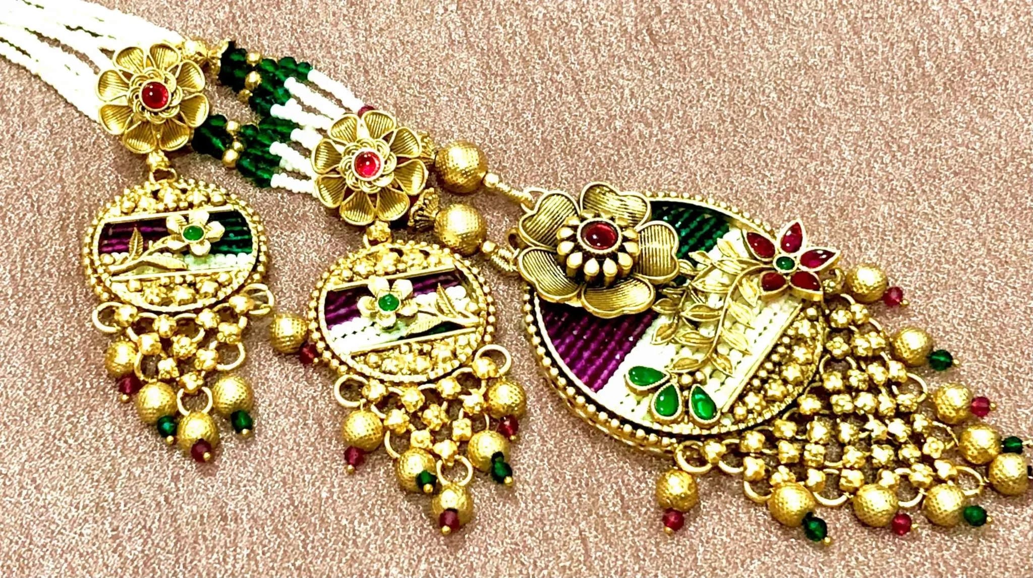 Traditional long golden Rajwadi Patwa necklace set with intricate floral motifs, green and red accents, and rice pearl detailing on a textured background