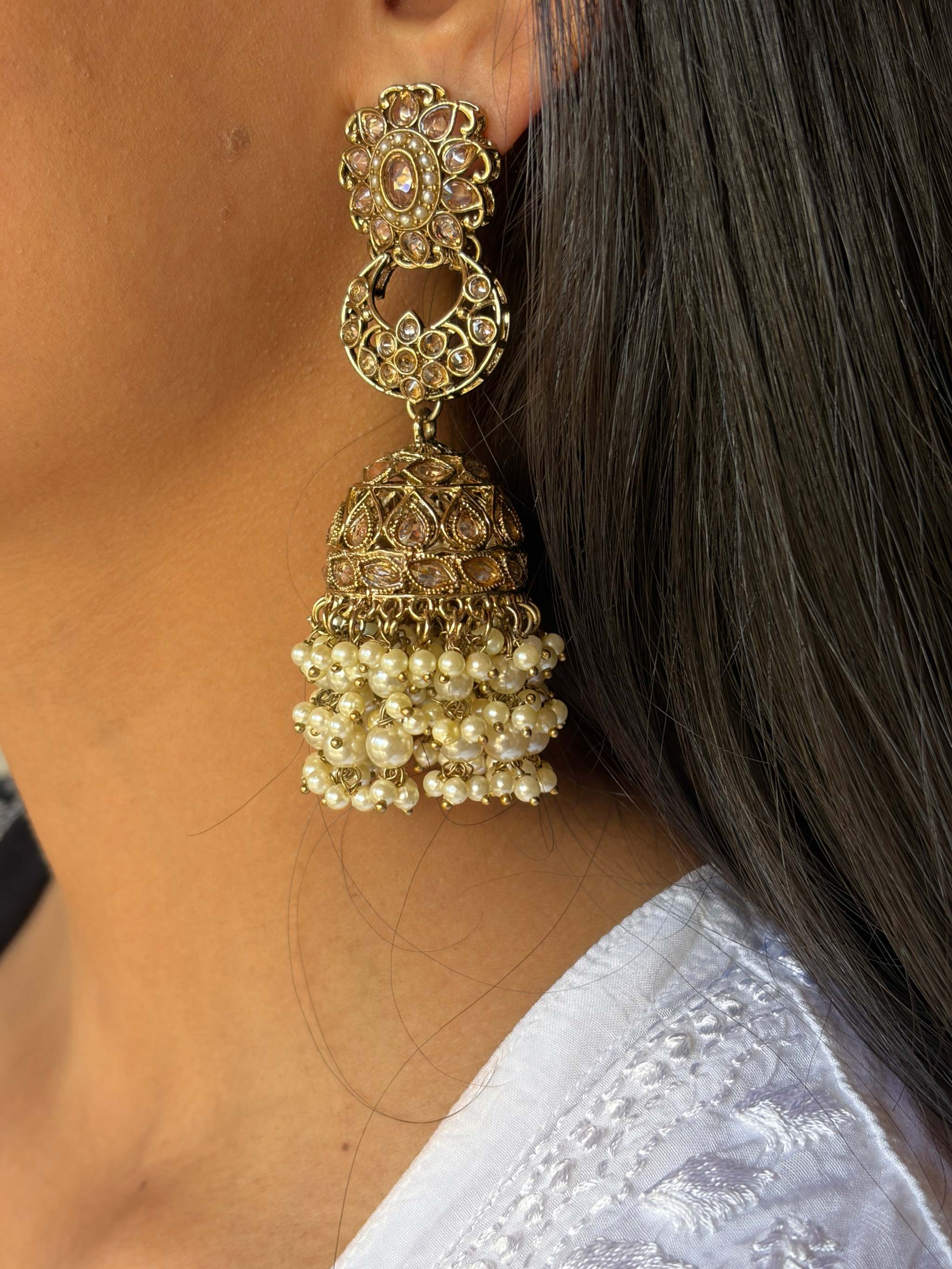 Close-up of a Moti Jhilmil Jhumke featuring intricate gold design with pearl clusters, worn on an ear.