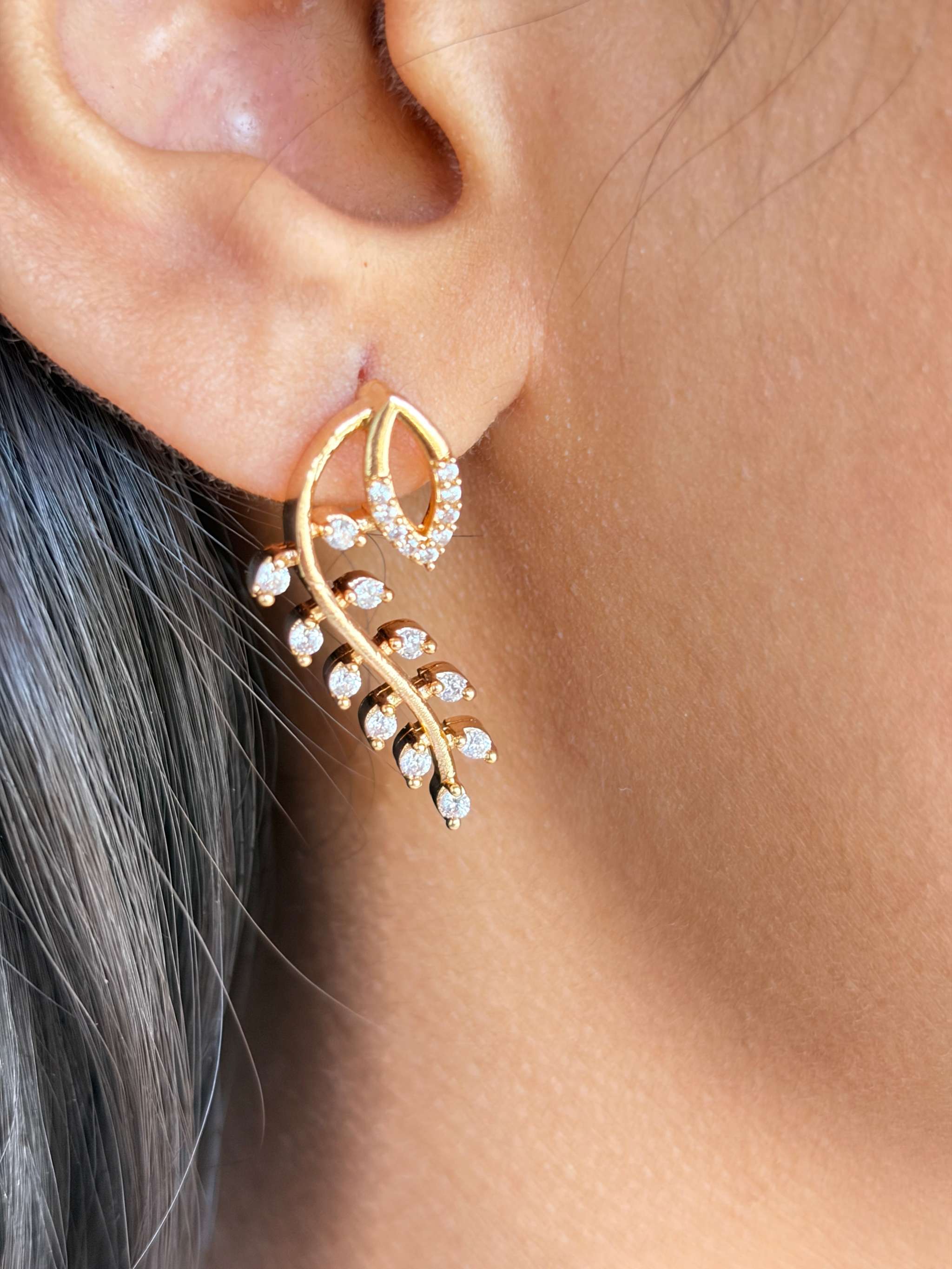 Close-up of Everglow Willow Necklace Set gold earring with leaf design and small sparkling stones on ear