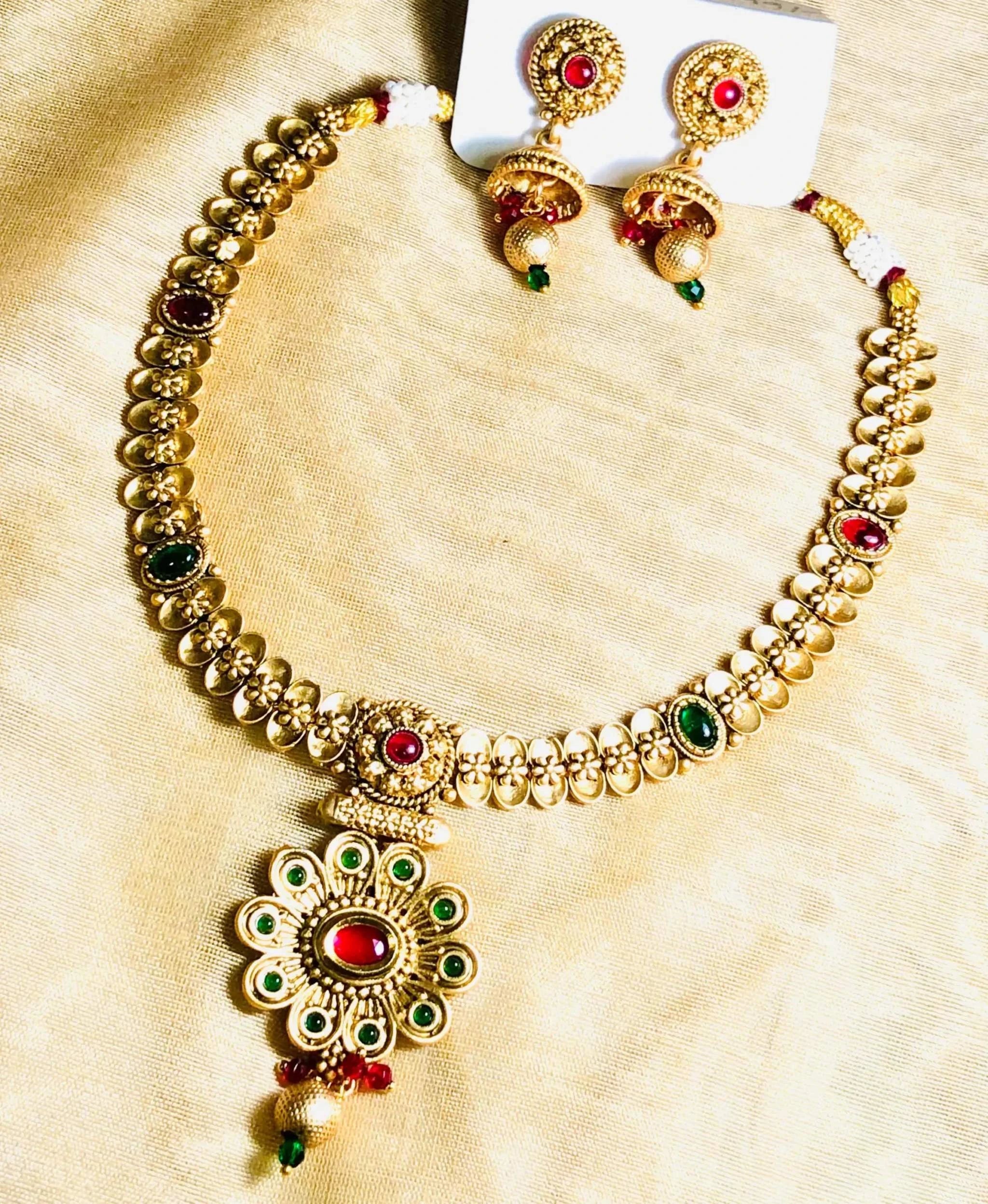 Rajwadi golden necklace set with intricate red and green Meenakari stones and matching earrings on a gold fabric background