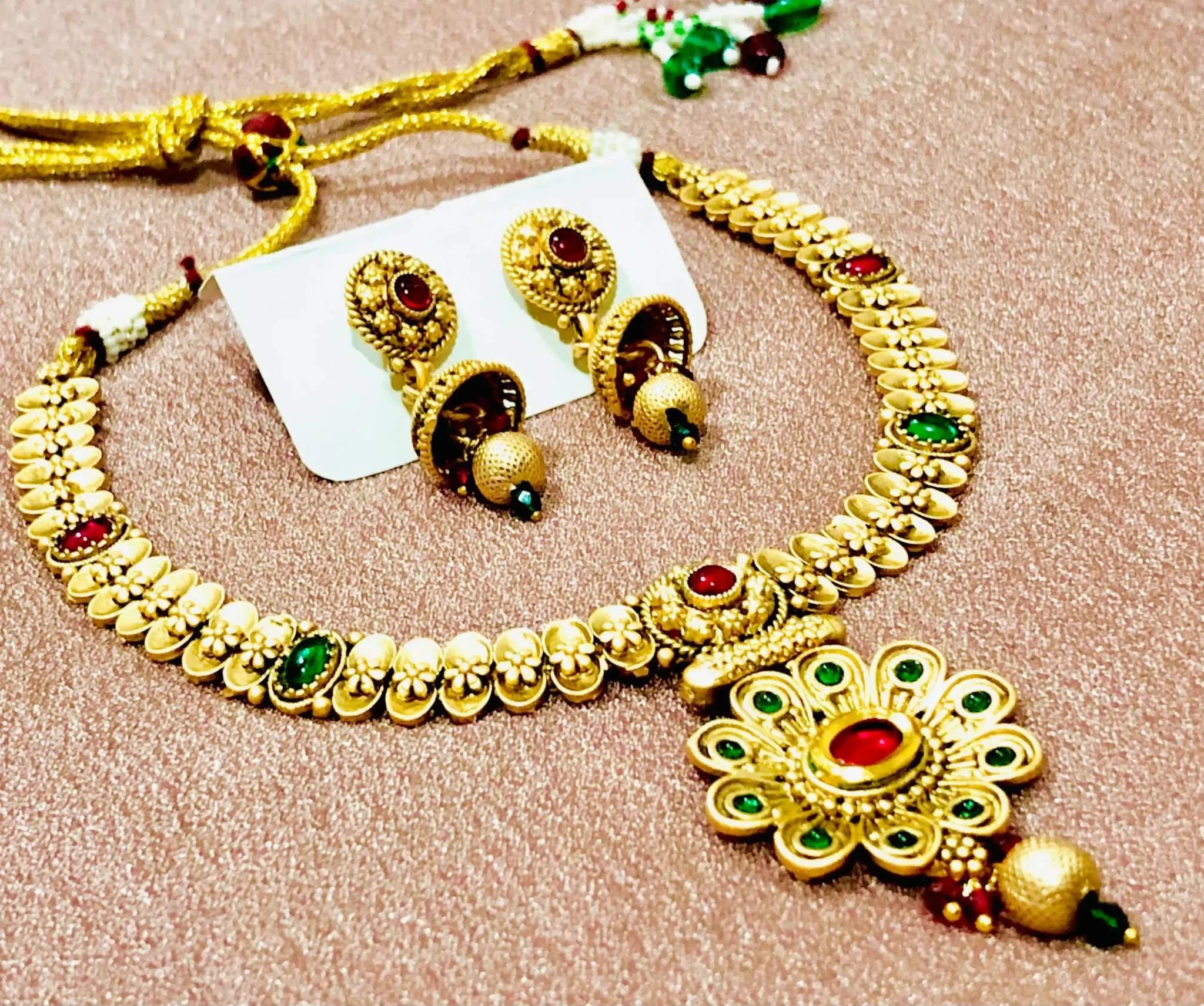 Rajwadi golden necklace set with intricate red and green meenakari stones and matching earrings on a textured surface