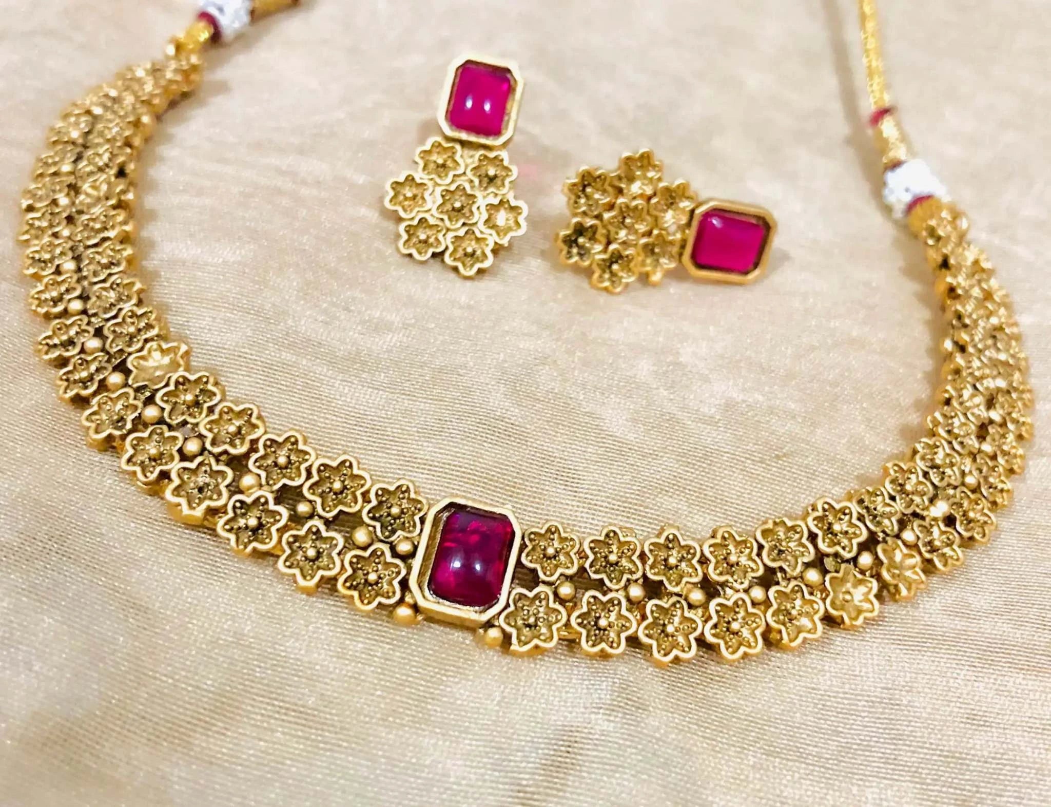 Golden Rajwadi Choker necklace set with intricate floral design and pink stone studs on a beige background