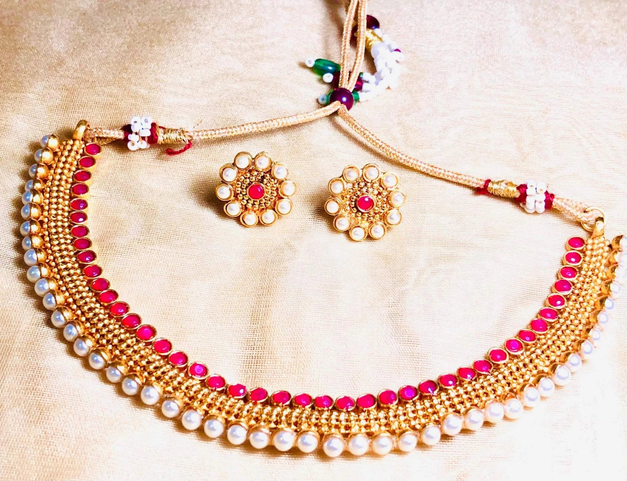 Traditional Pearl and Coral Rajwadi Necklace Set featuring intricate gold design with red coral stones and pearl accents, paired with matching stud earrings on beige fabric background