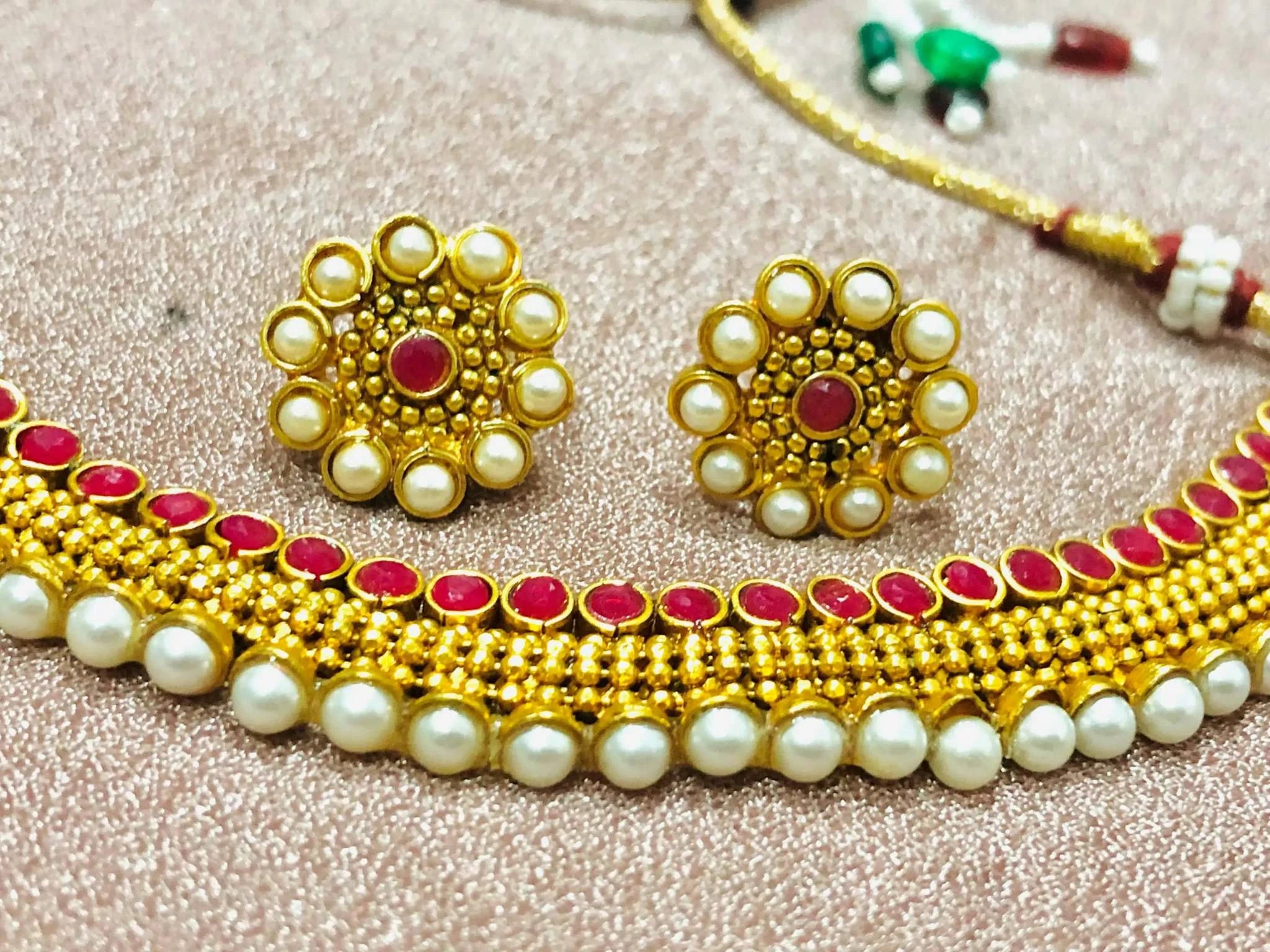 Traditional Pearl and Coral Rajwadi Necklace Set with intricate gold designs and matching pearl and coral stud earrings on a textured surface