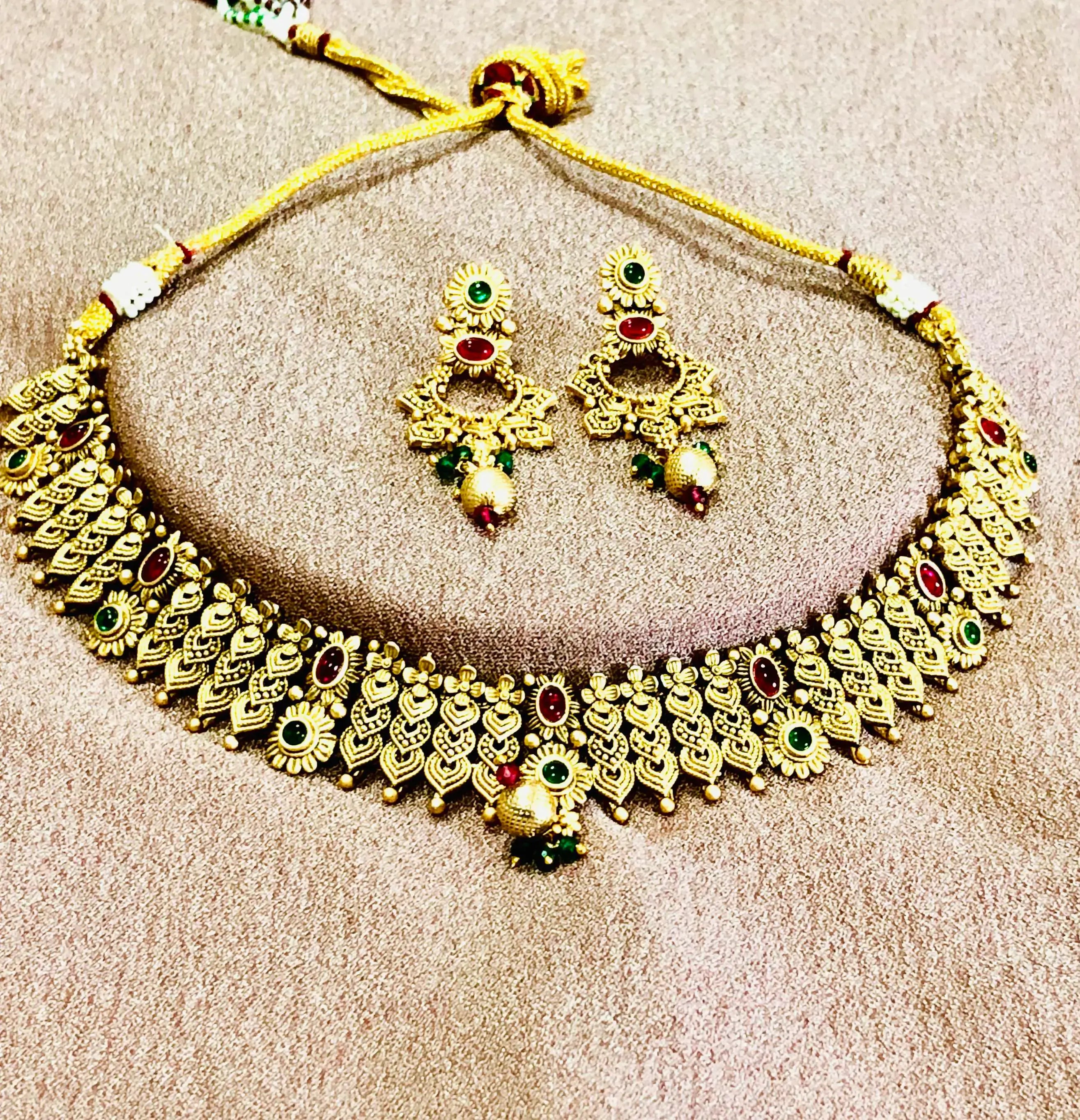Gold-toned necklace and earring set with red and green stones, adjustable cord.