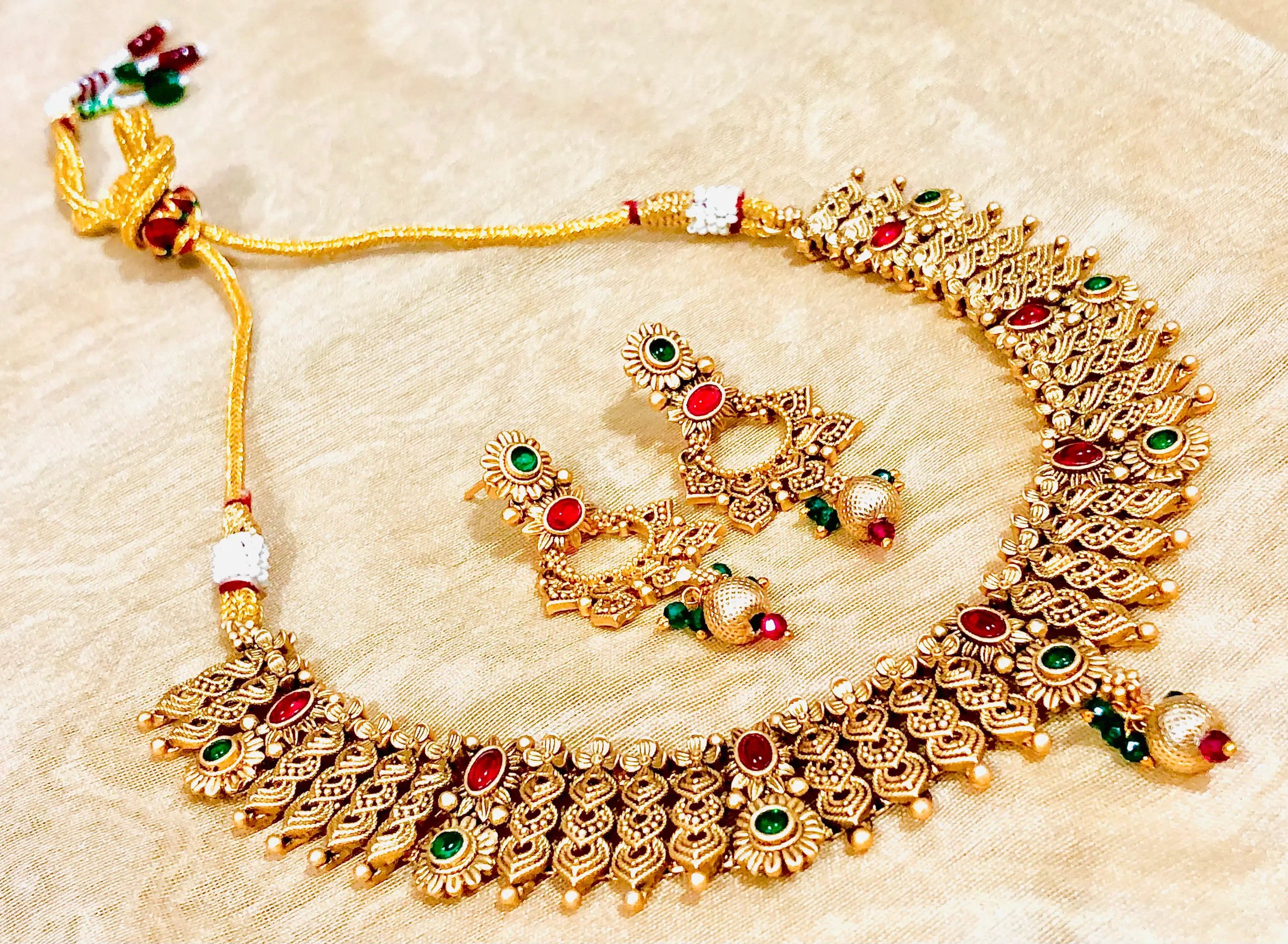 Gold Indian jewelry set with necklace and earrings, featuring red and green stones.