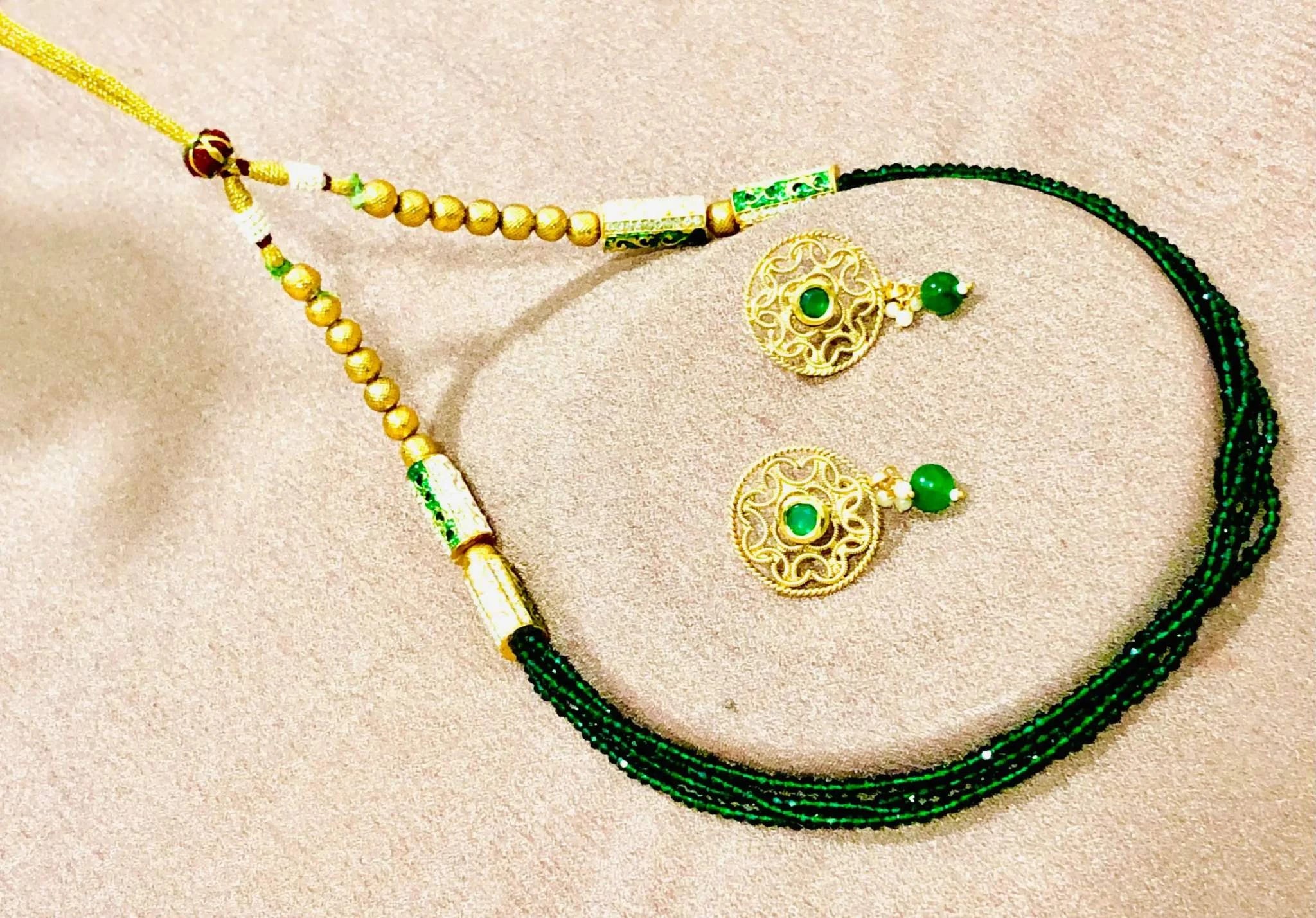Golden and Emerald beaded jewelry set with round earrings and multi-strand emerald necklace on beige background