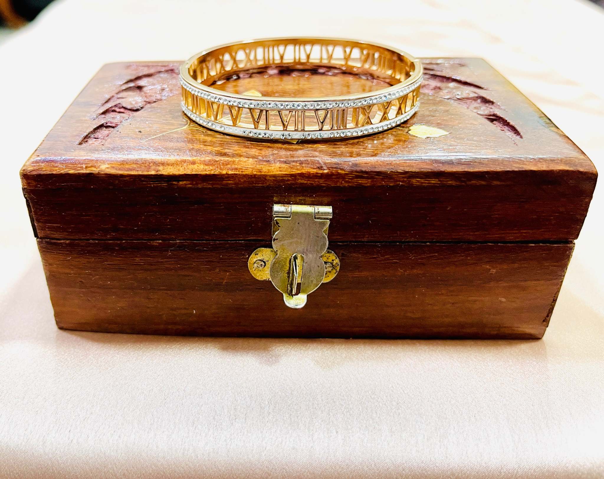 Rose gold bracelet with engraved Roman numerals displayed on a wooden box