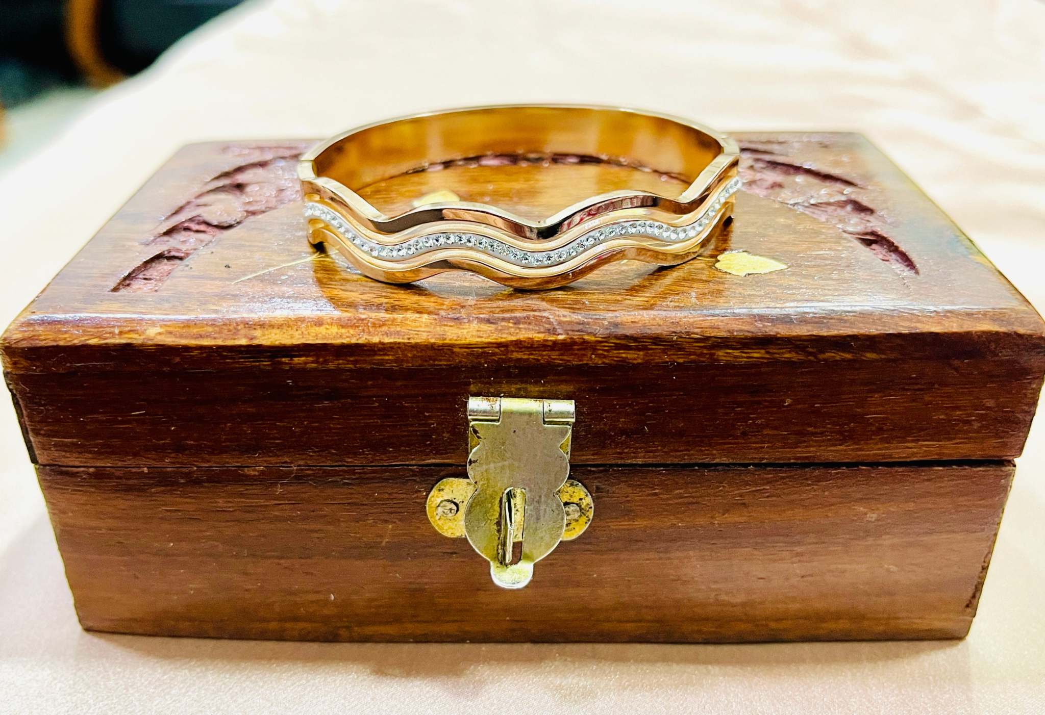 Rose gold bracelet with diamond-accented wave design on wooden box