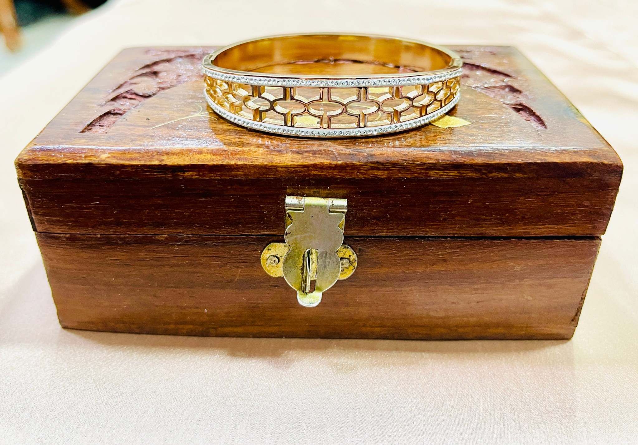 Gold intricate jali work bracelet with diamond accents on wooden jewelry box