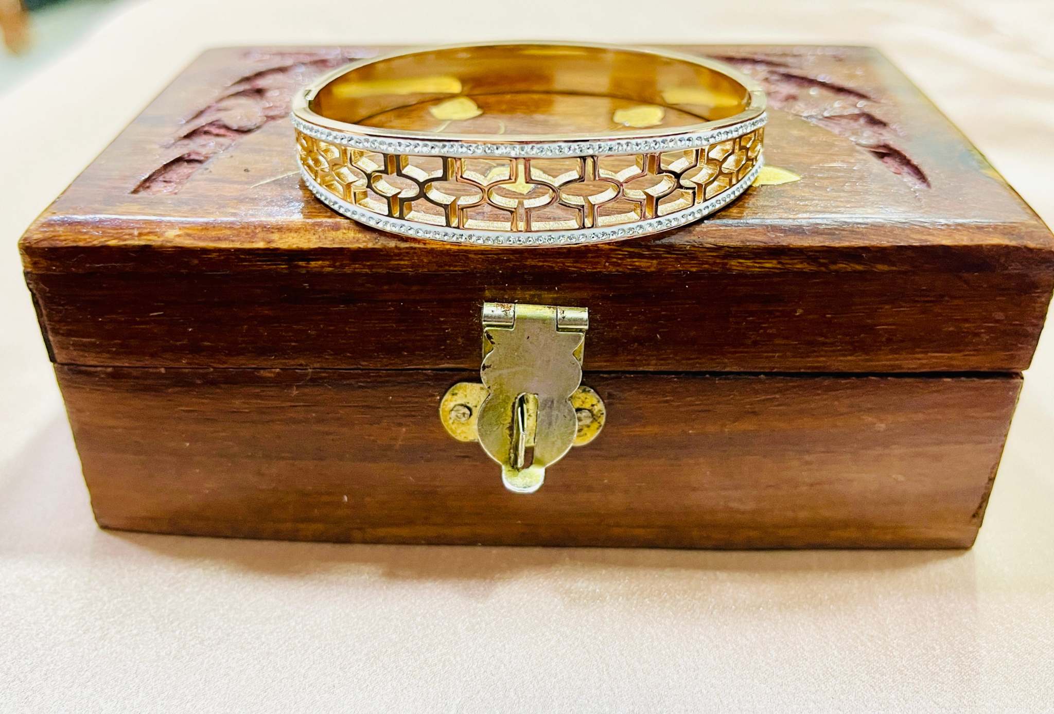 Gold intricate jali work bracelet with diamond accents on wooden jewelry box