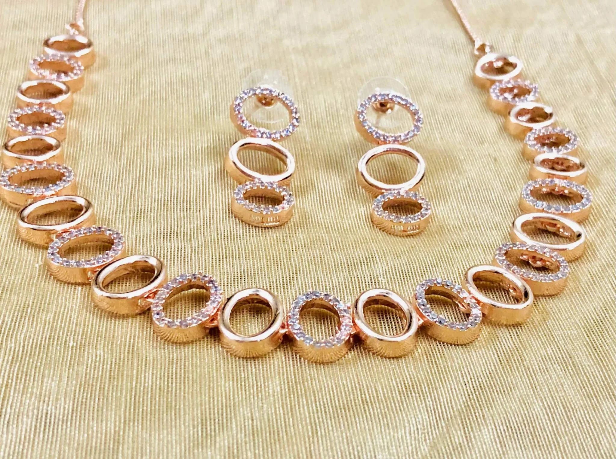 Rose gold oval earrings and matching necklace set adorned with sparkling crystals on gold fabric background