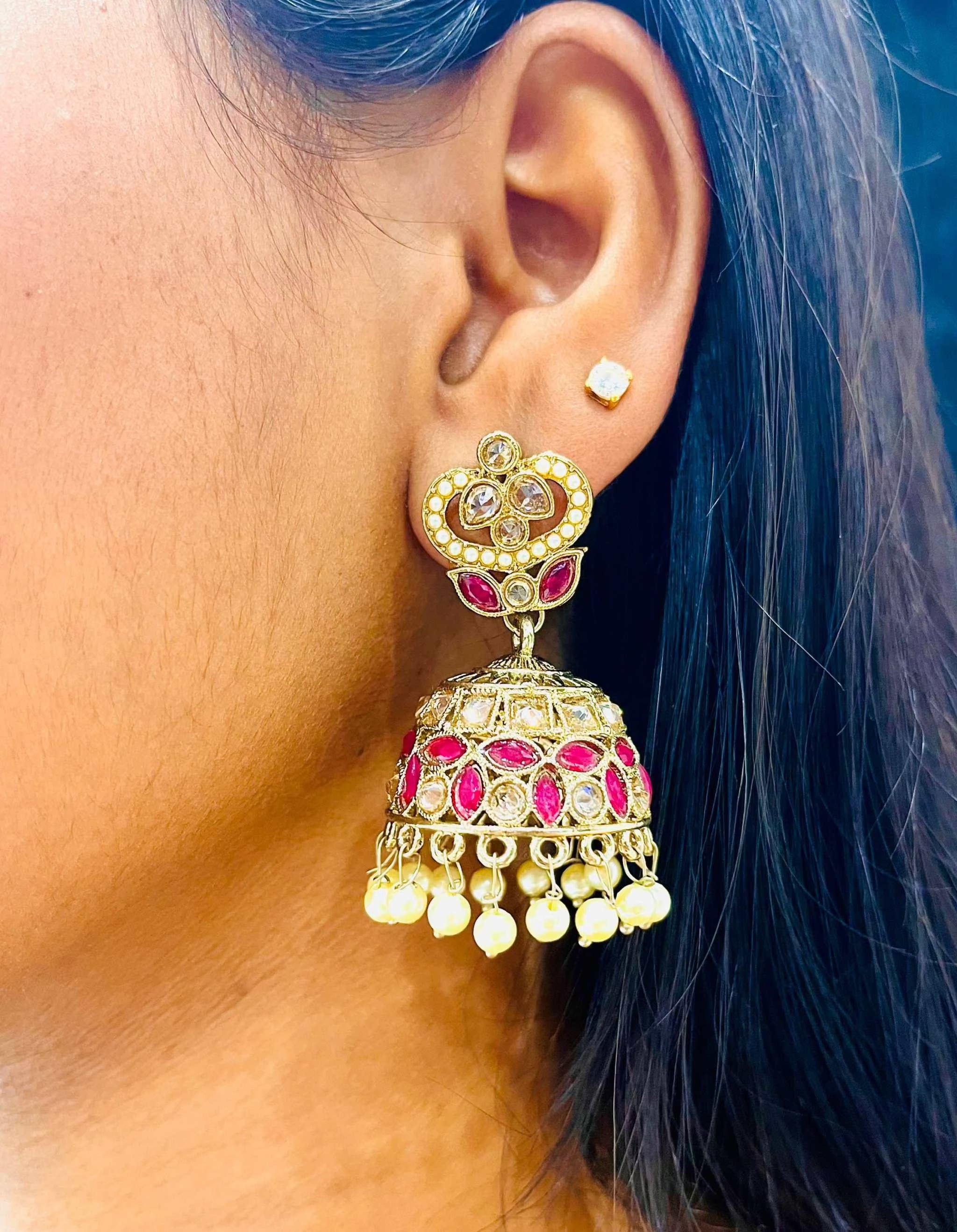 Close-up of a woman's ear wearing Rani Pink Taj Jhumkas with intricate gold detailing and pink embellishments