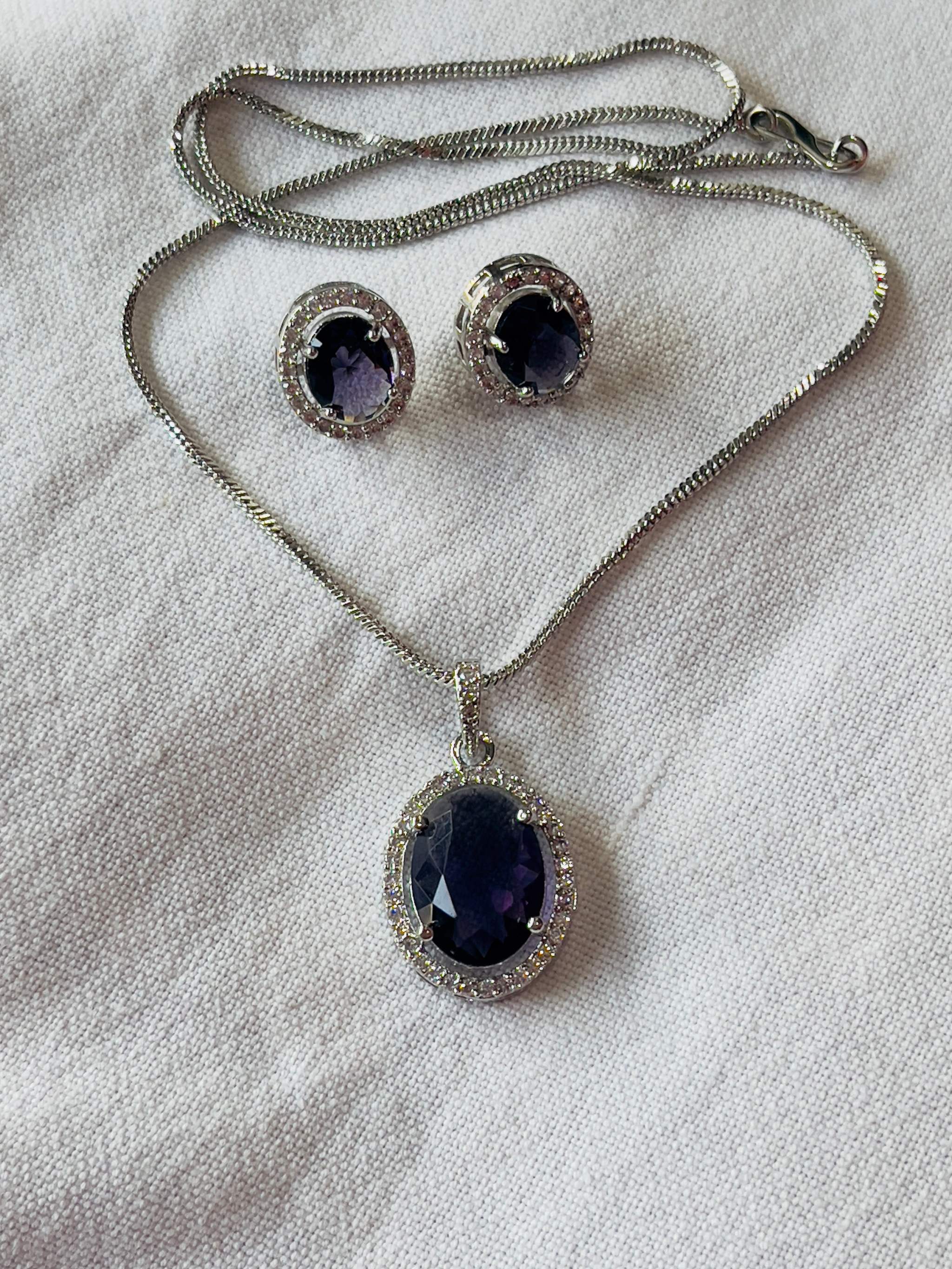 Violet oval gemstone pendant and matching earrings set with silver chain and halo setting