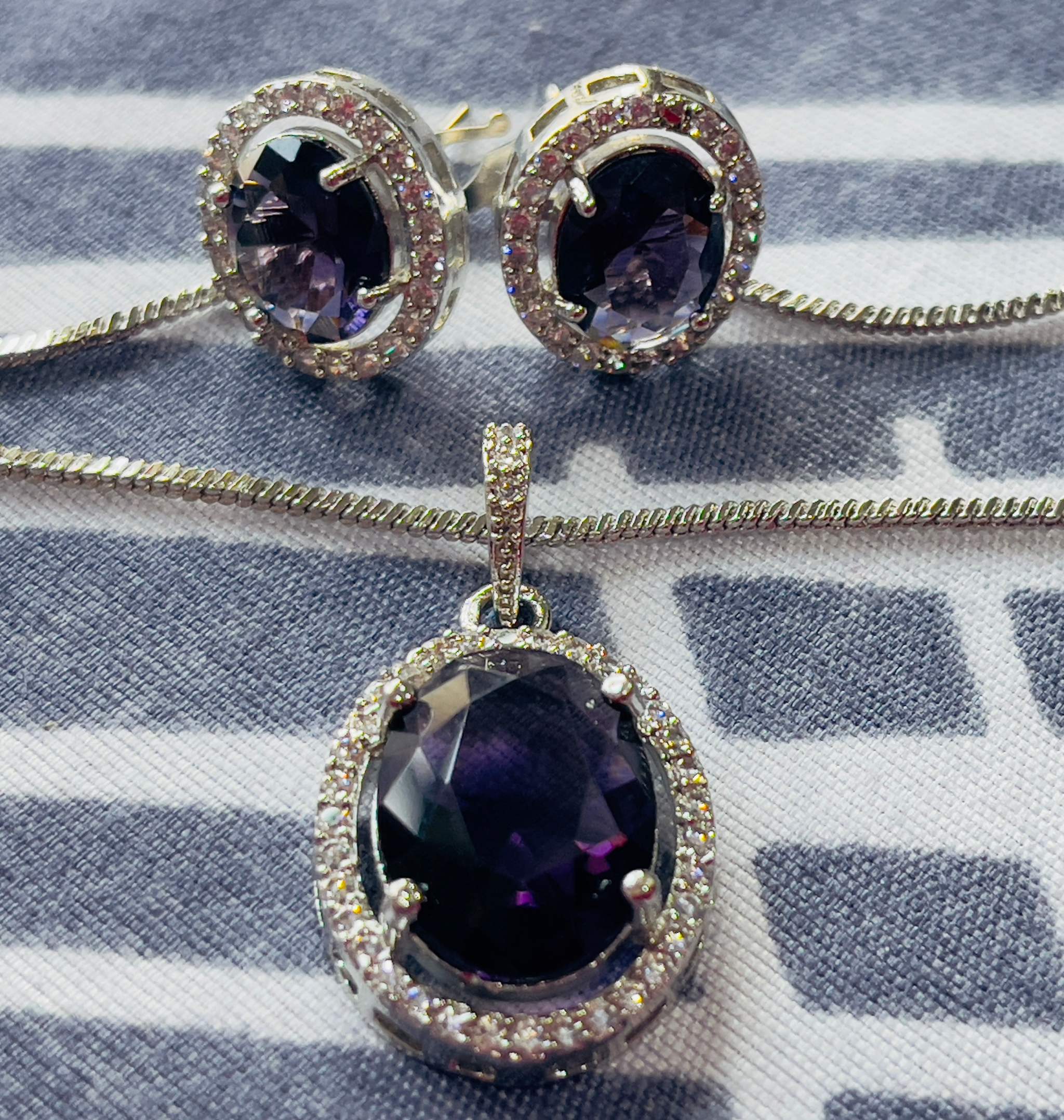 Violet Oval Grand Pendant Set with deep violet oval gemstone surrounded by small sparkling stones in silver setting including matching earrings and pendant necklace