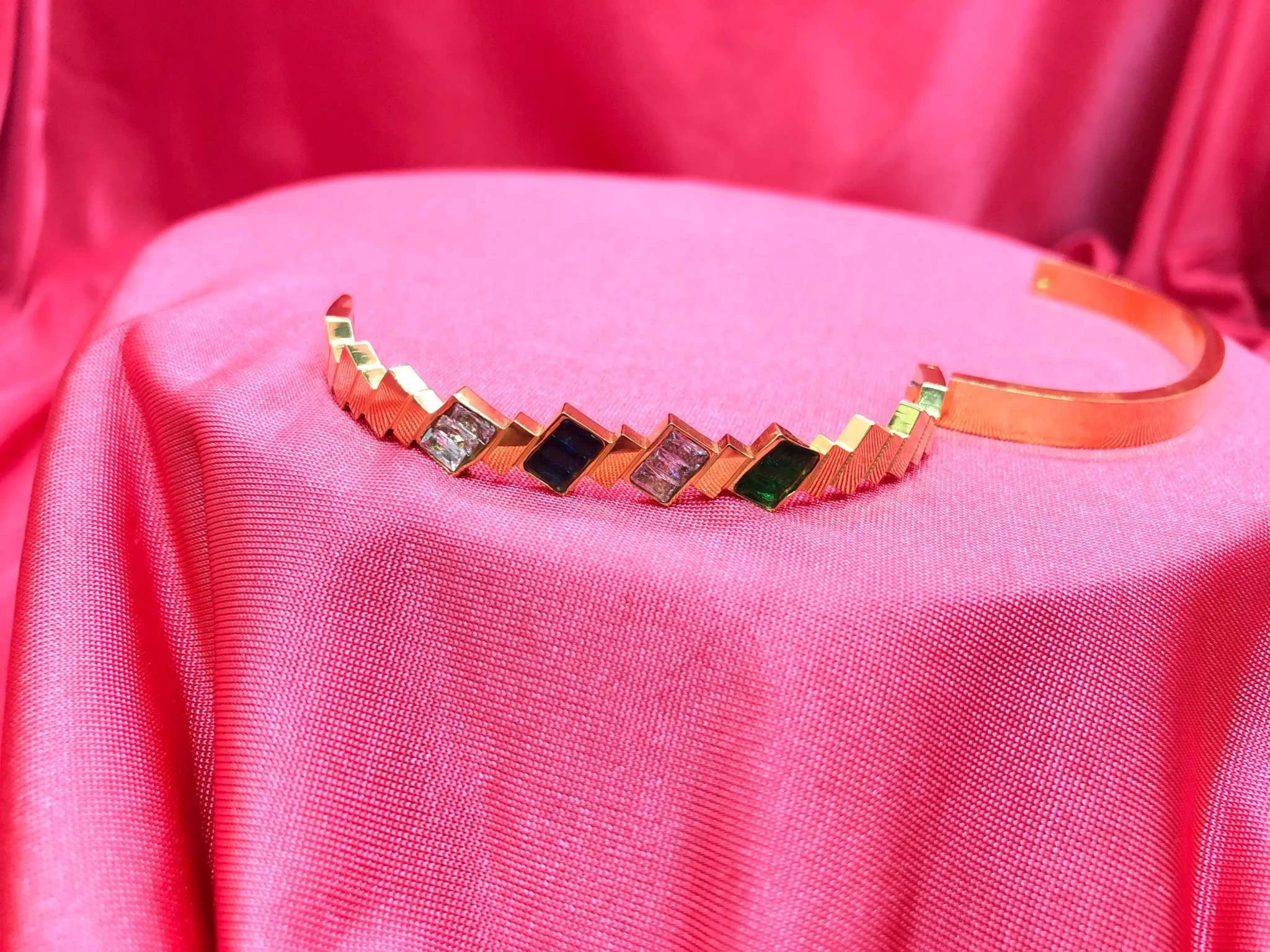 Elegant gold Korean bracelet with multicolor stones and diamond look displayed on pink fabric background