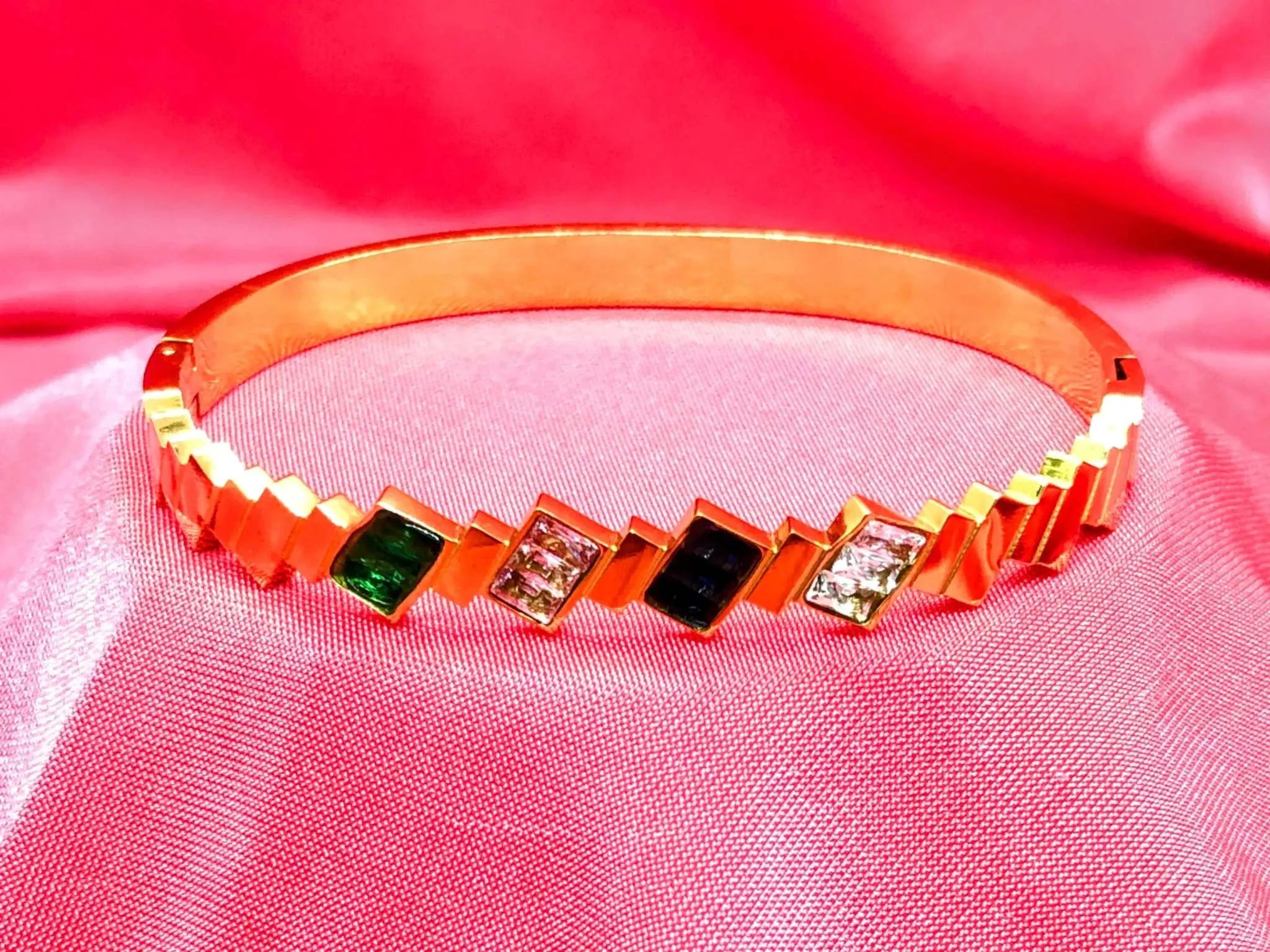 Elegant gold Korean bracelet with multicolor stones and diamond-like accents on pink fabric background