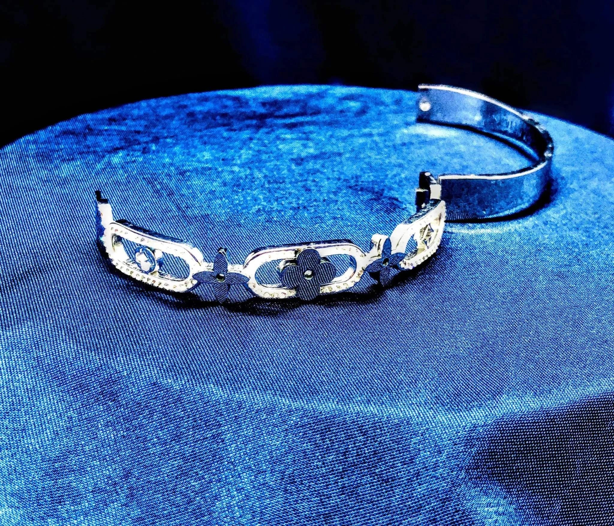 Elegant silver bracelet with white diamond stones and floral design on blue fabric background