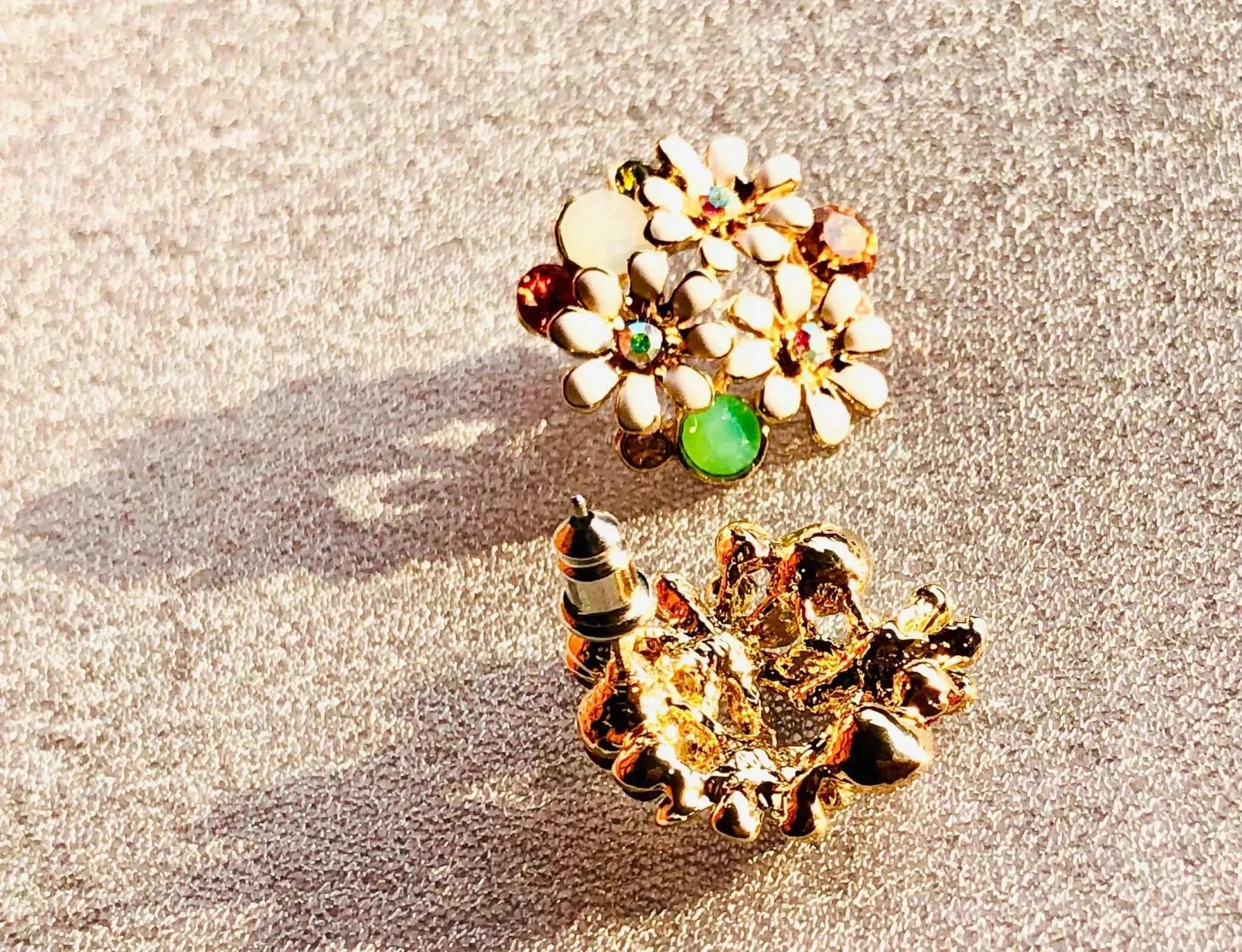 Rose gold floral stud earrings with white enamel petals and multicolored gemstone accents