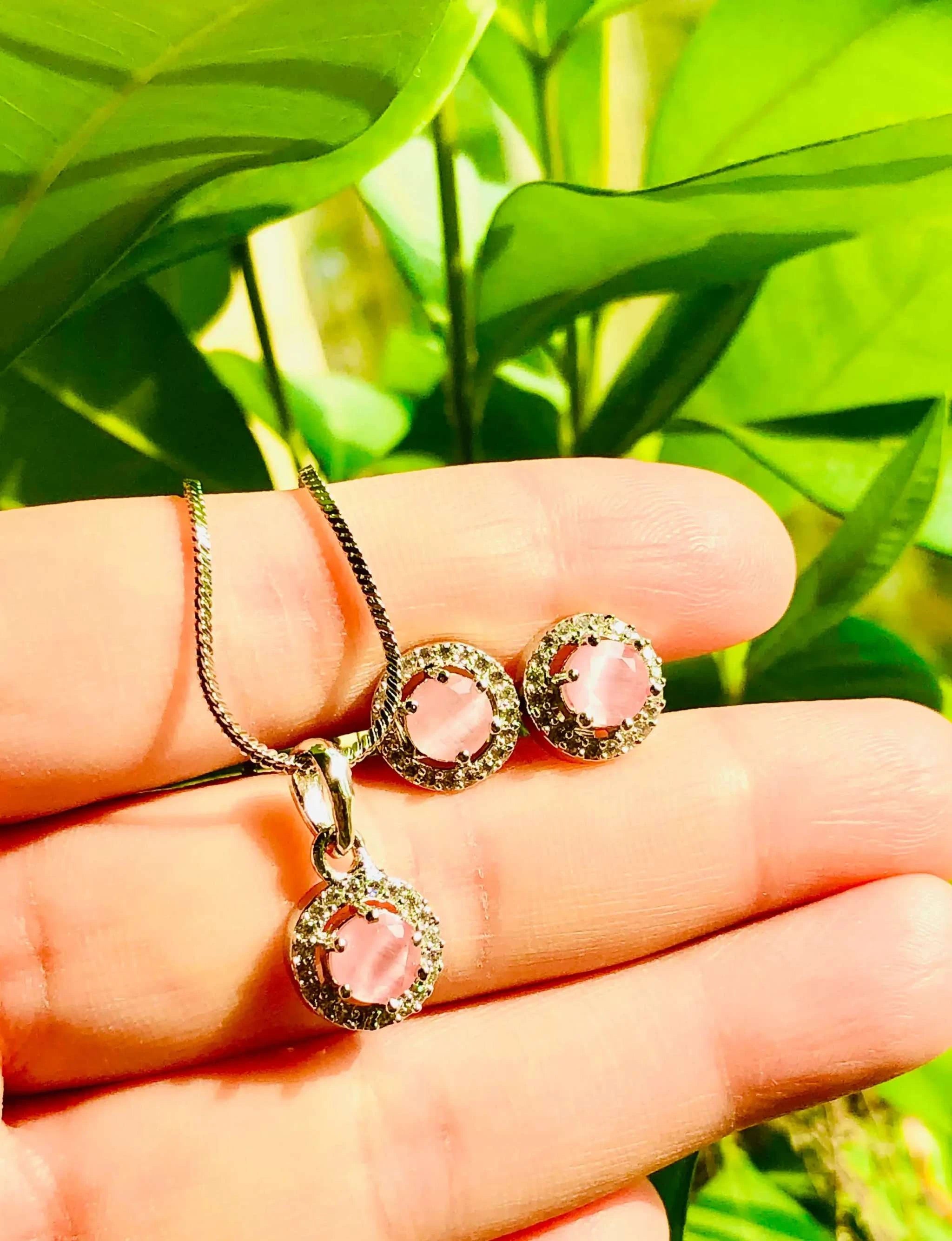 Charming baby pink silver earrings set with round pendant and sparkling finish in hand against green leaves background