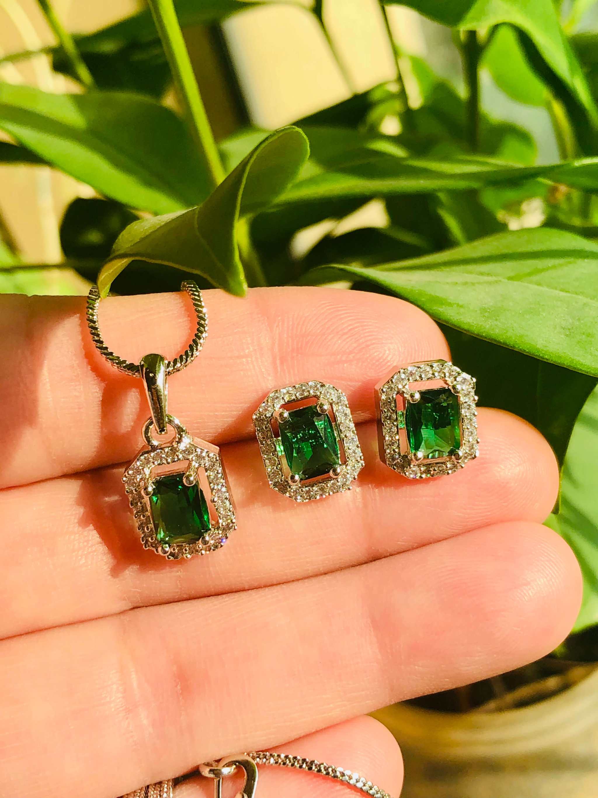 Green emerald and white AD rectangle pendant and earrings set on hand with green leaves background