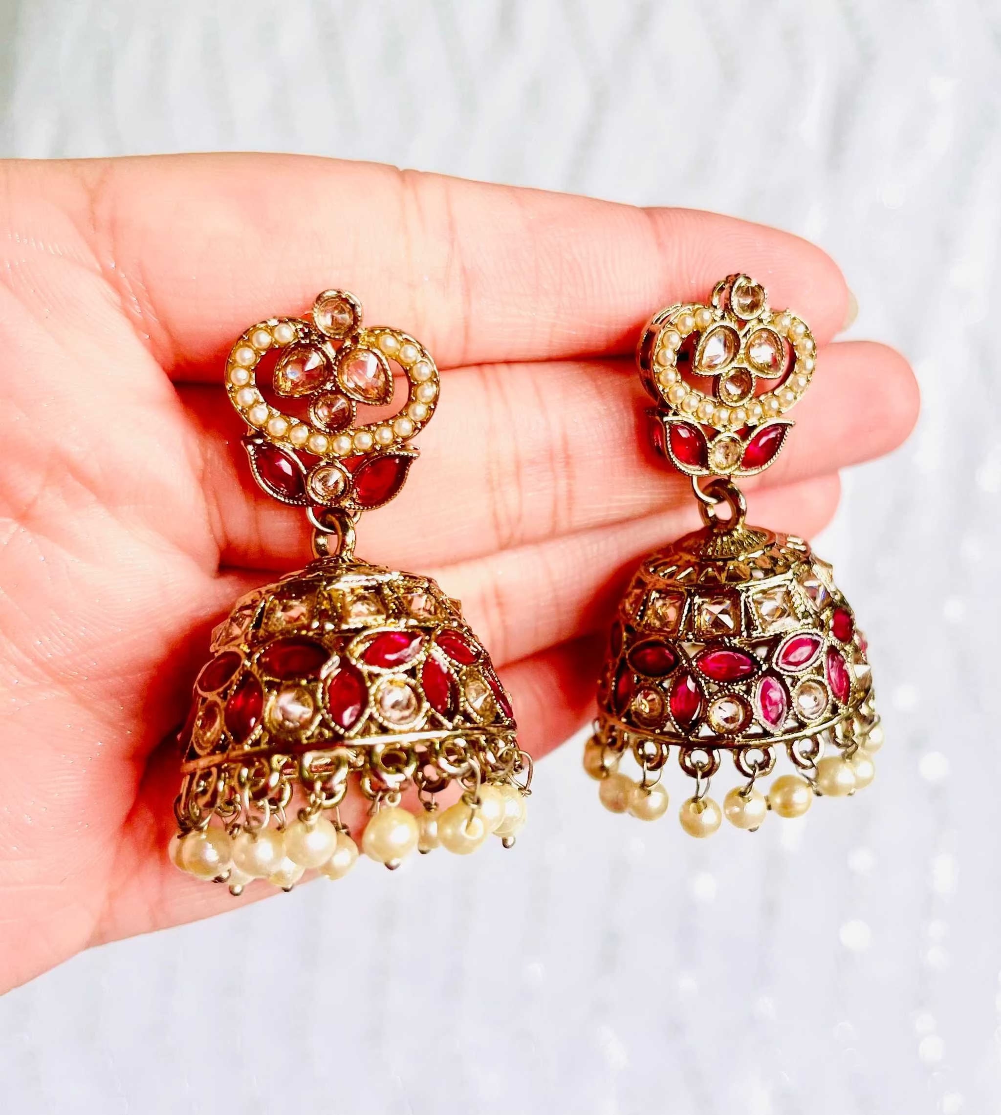 Rani Pink Taj Jhumkas with intricate gold detailing, pink gemstones, and pearl drops, held in hand against a white background